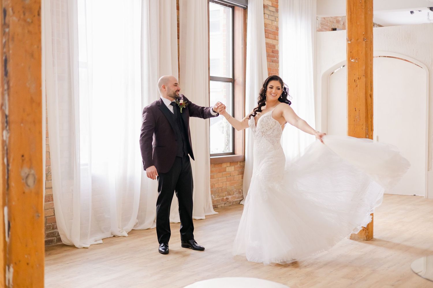 A couple dances together in a bright loft space with wooden beams and white curtains.