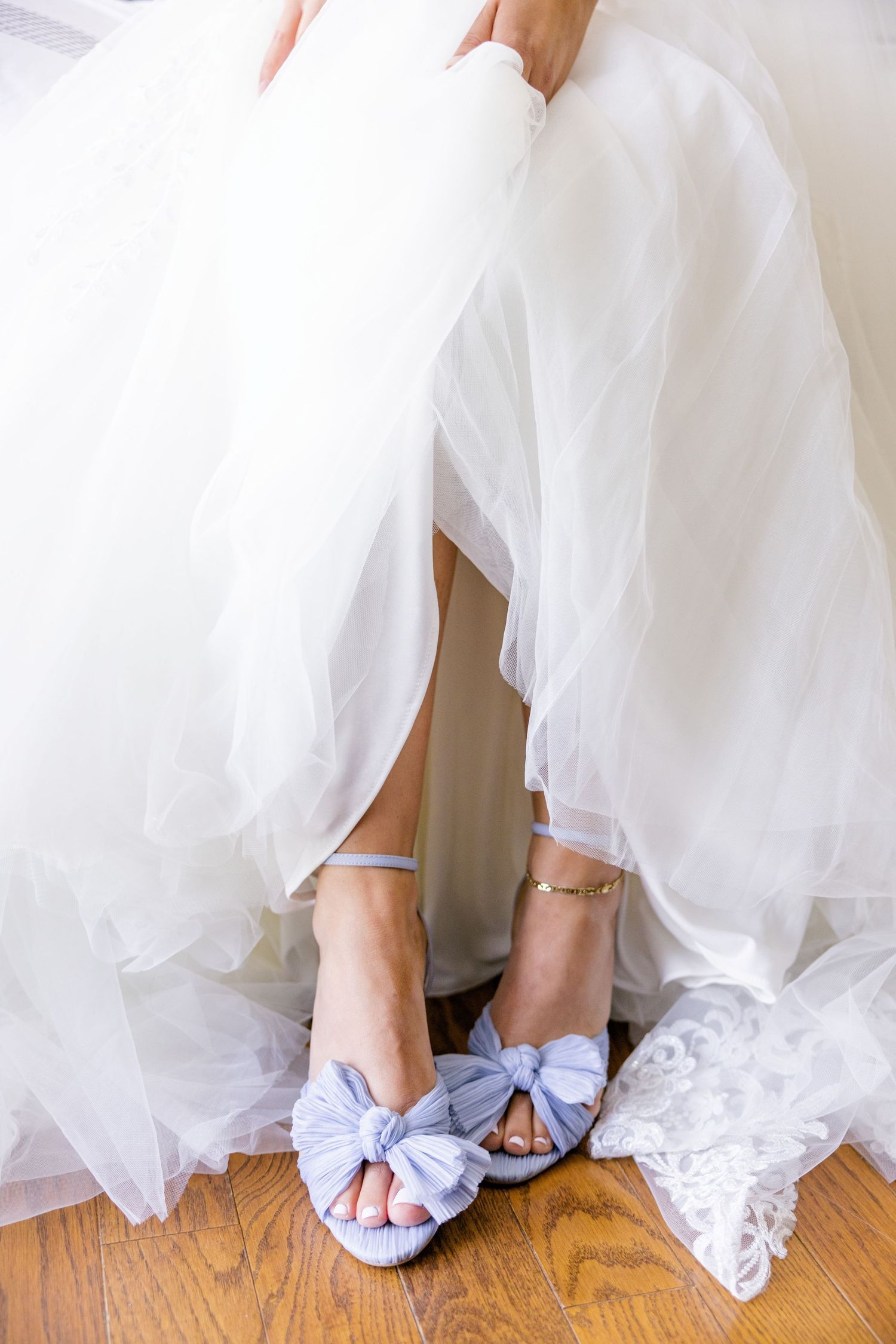 Close-up of light blue bow wedding shoes under flowing white tulle dress.