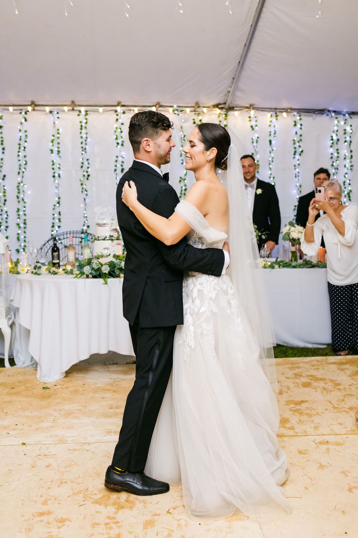 Couple shares intimate dance moment under tent with string light and floral decorations.