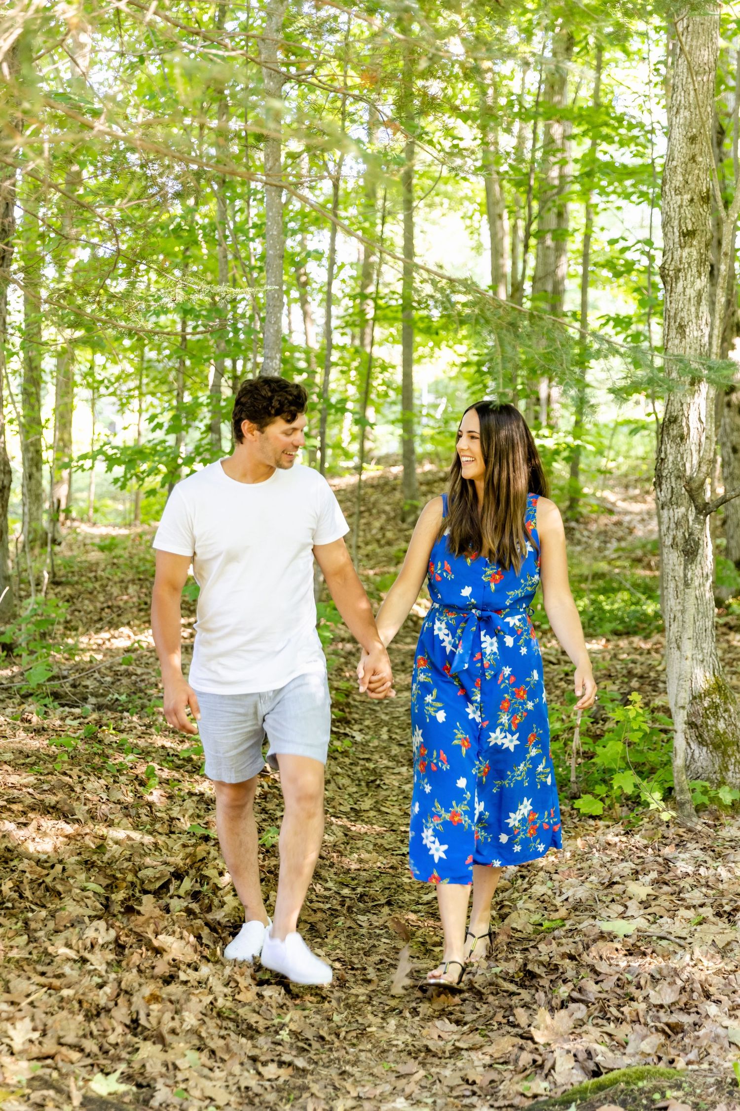 Couple walking hand in hand along a forest trail wearing casual summer attire.
