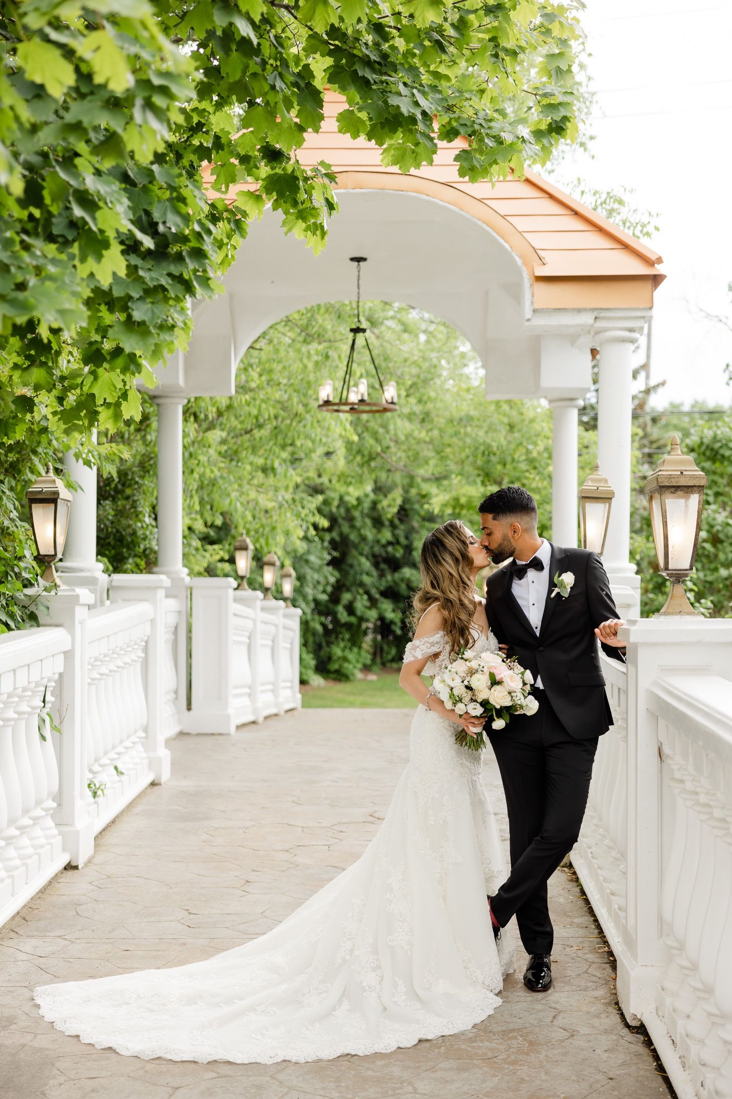 Elegant couple shares intimate moment on columned walkway with trailing wedding gown.