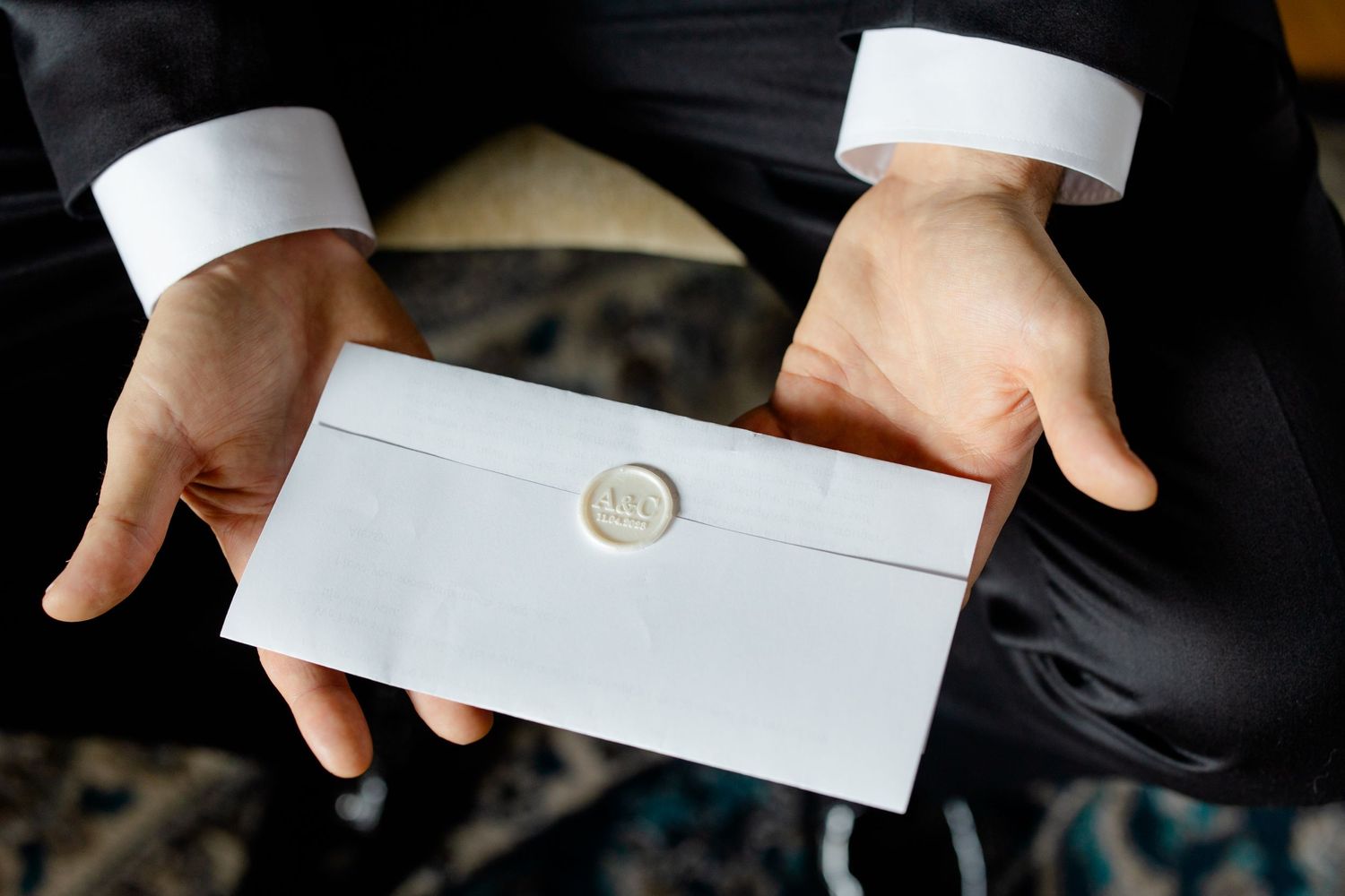 White envelope with wax seal being held by hands in formal dress shirt cuffs.