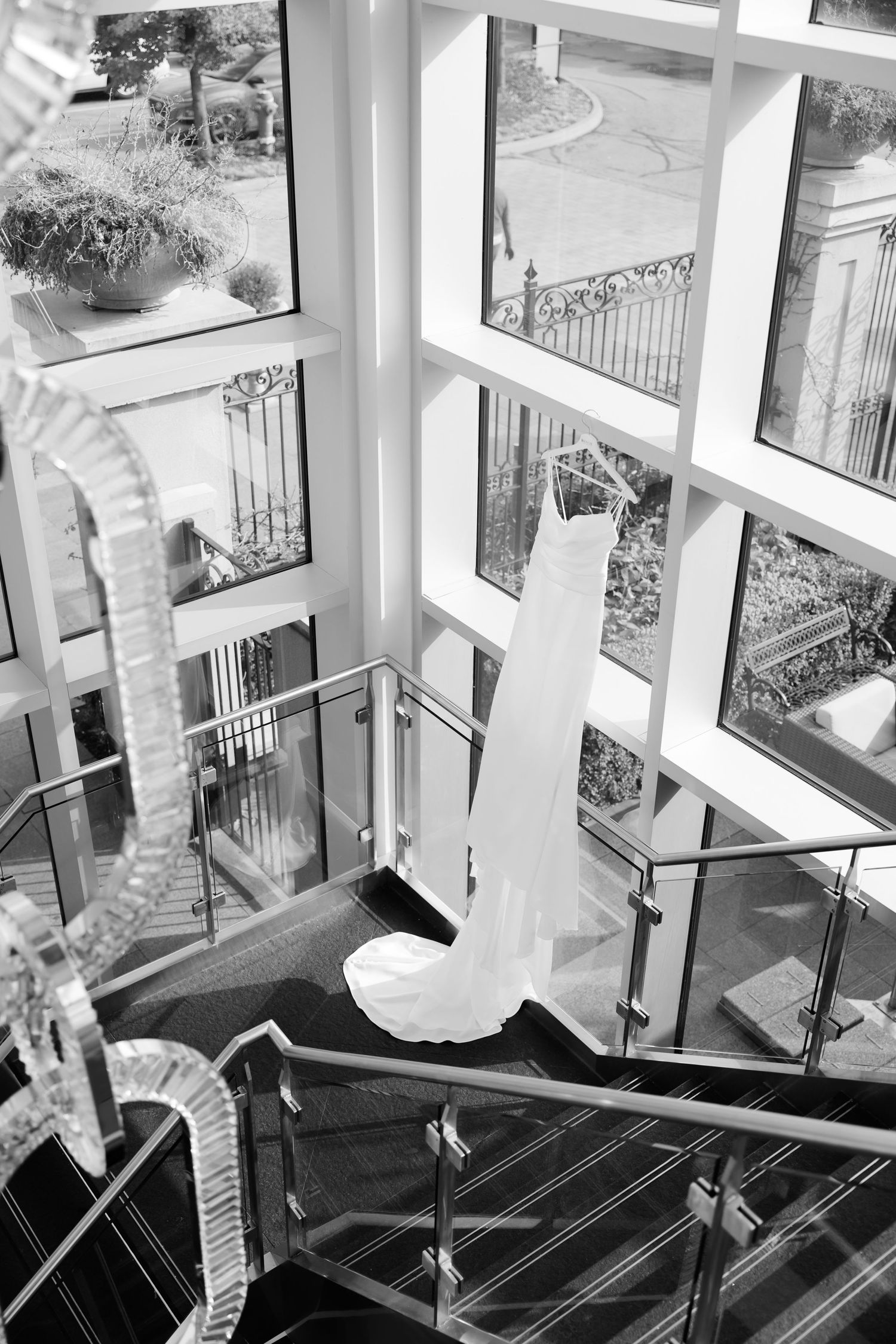 Black and white photo of wedding dress suspended in modern stairwell with window views.