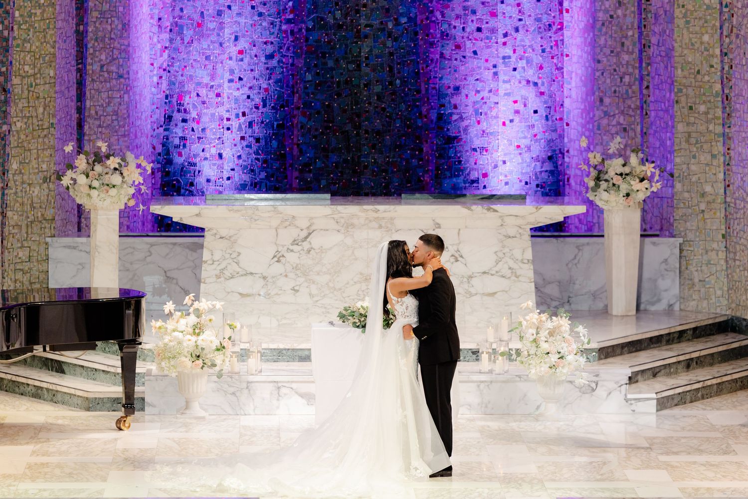 Couple sharing first dance on marble platform with purple uplighting and floral decorations.