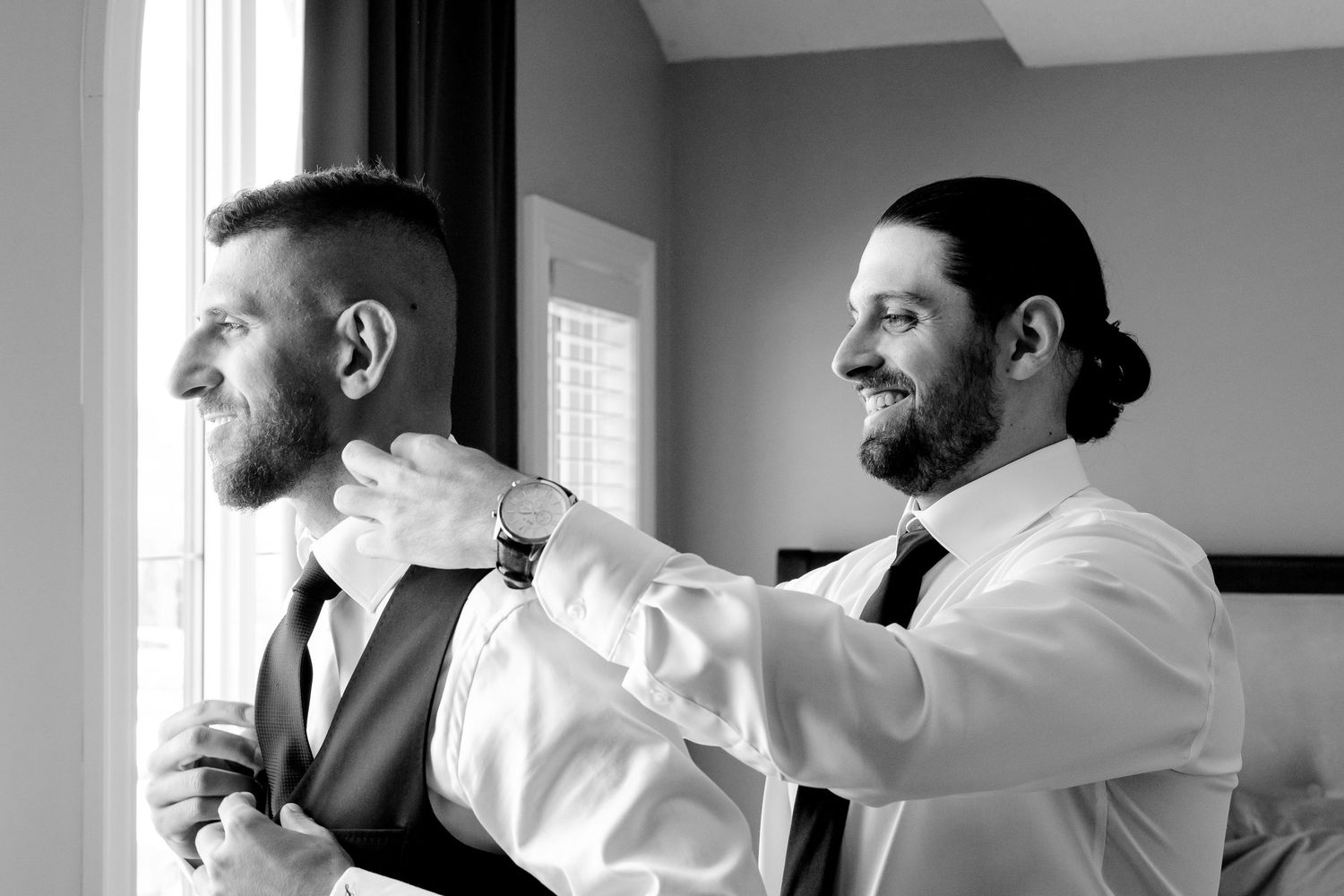 Two people in white shirts assisting with formal wear preparations.