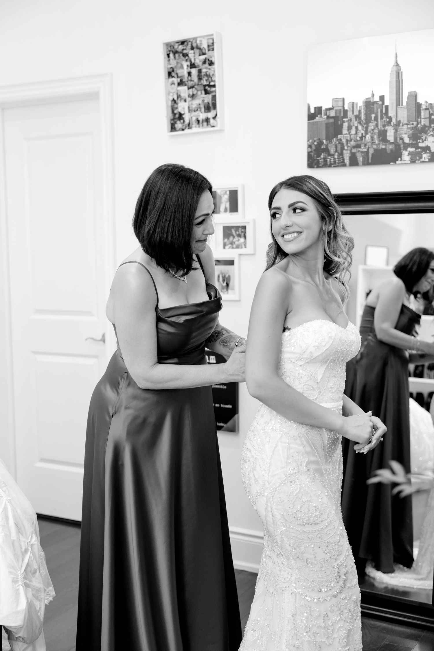 Black and white photo of wedding preparation with bride in dress and attendant in dark gown.