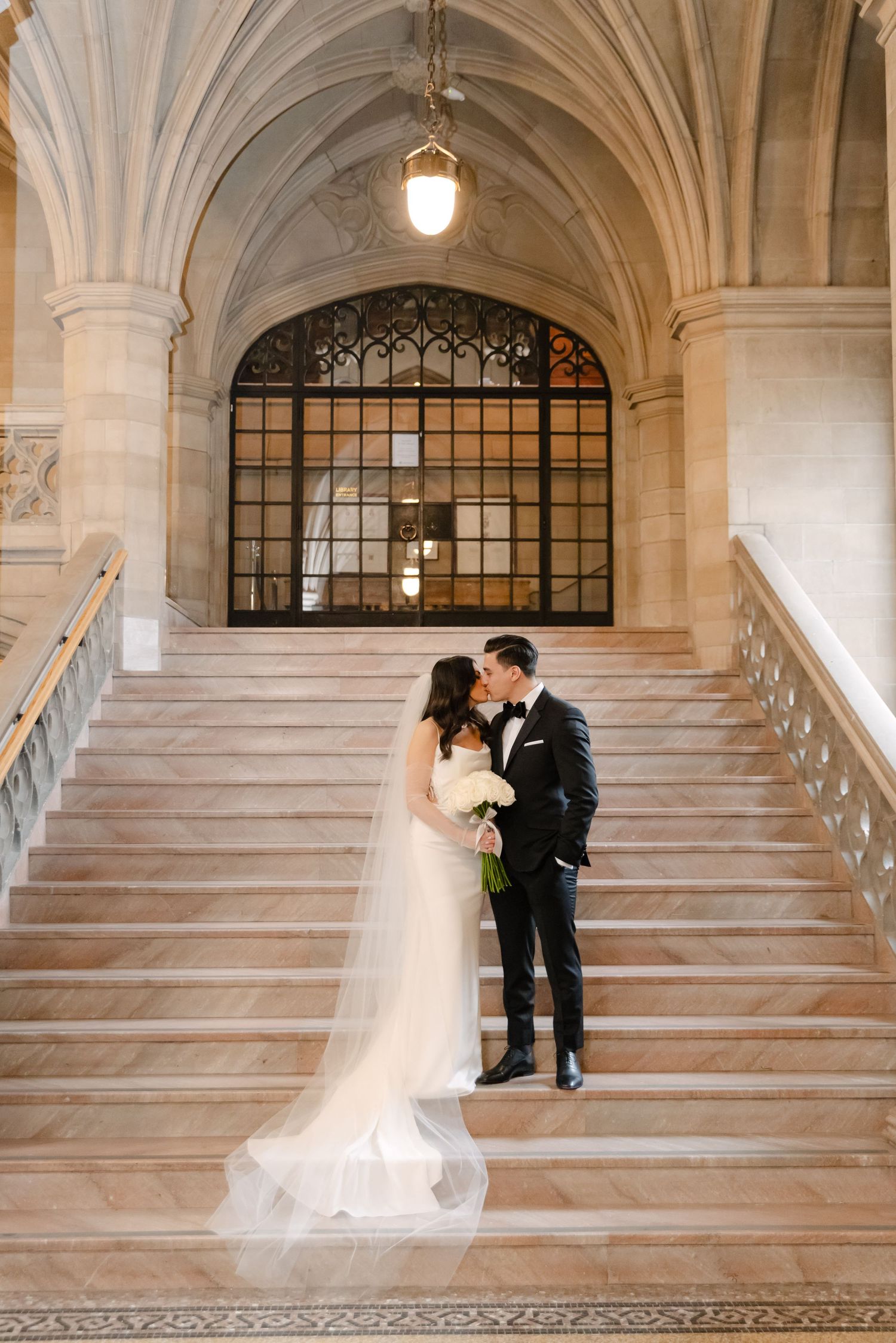 Intimate wedding portrait on elegant stone staircase with gothic architectural details and pendant lighting.