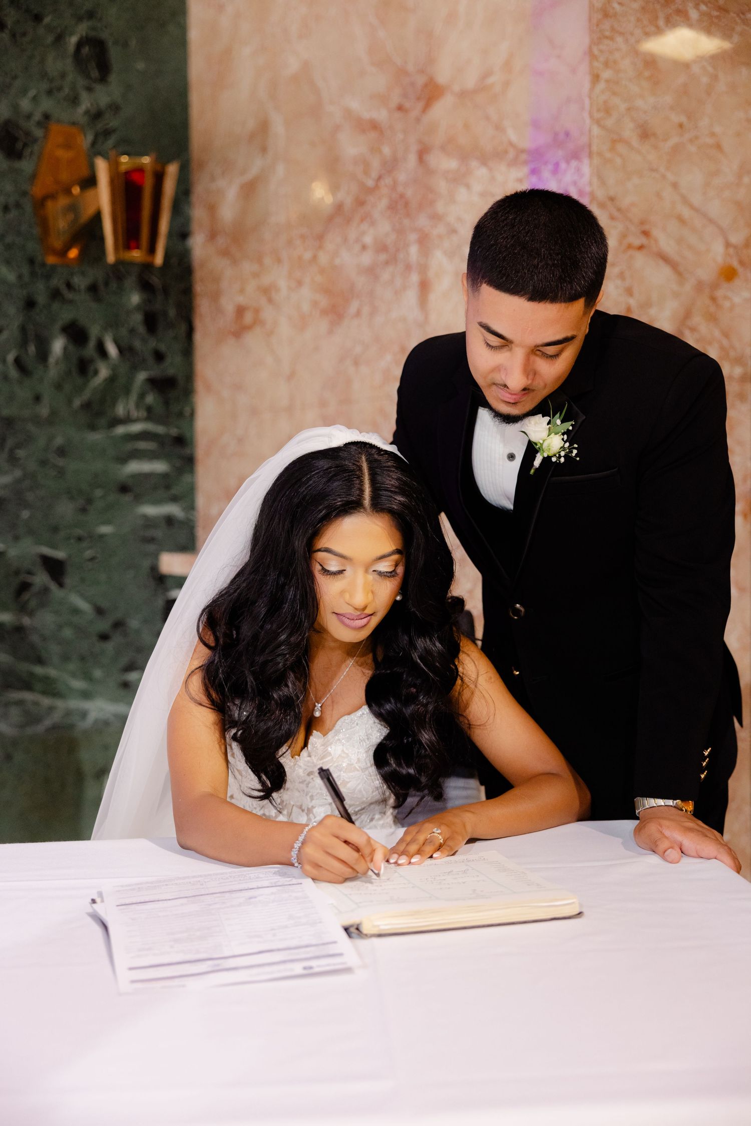 Bride signing marriage certificate at white table with elegant decor.