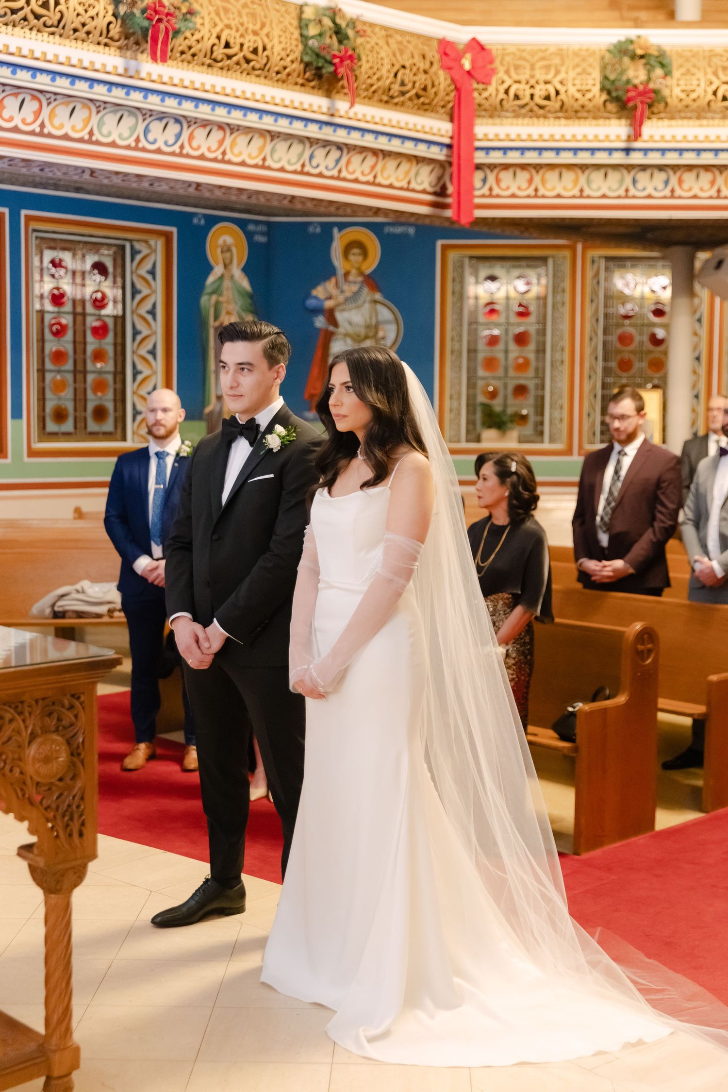 Wedding ceremony in ornate orthodox church with gold trim and religious icons on blue walls.