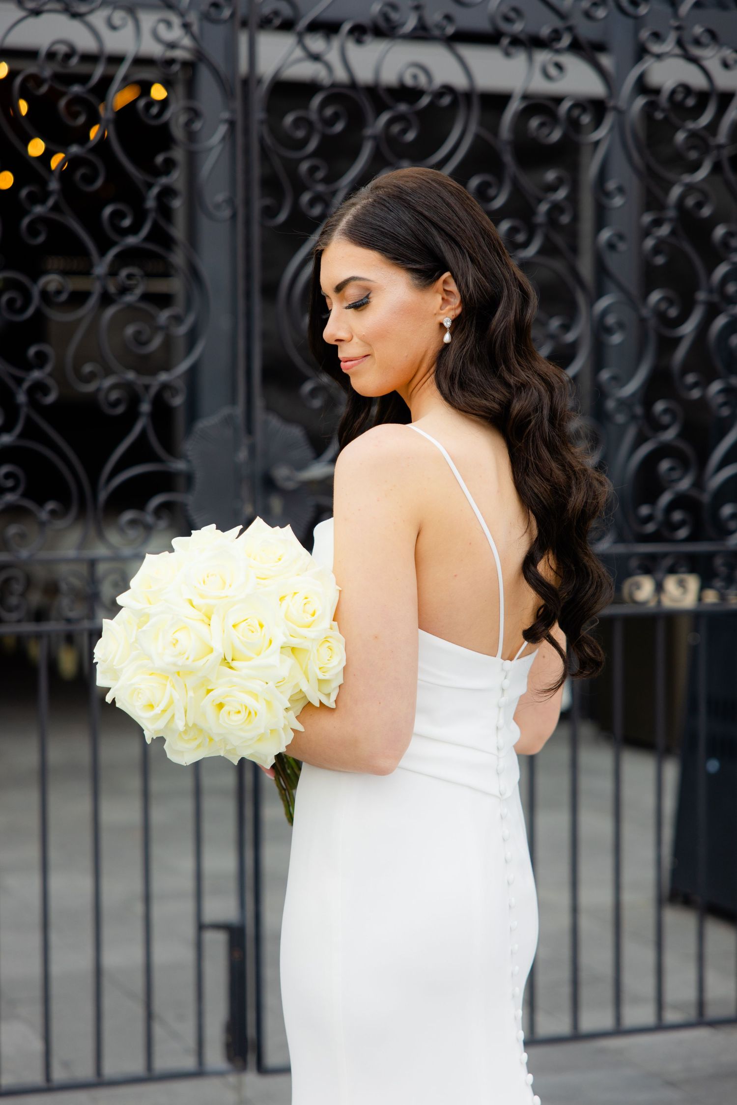 Bride holds cream rose bouquet while posing against ornate black iron gate.