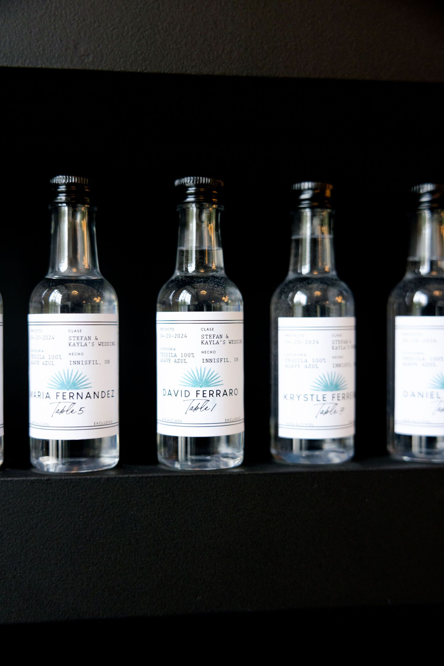 Close-up of clear glass bottles with white labels arranged in a row on a dark shelf.