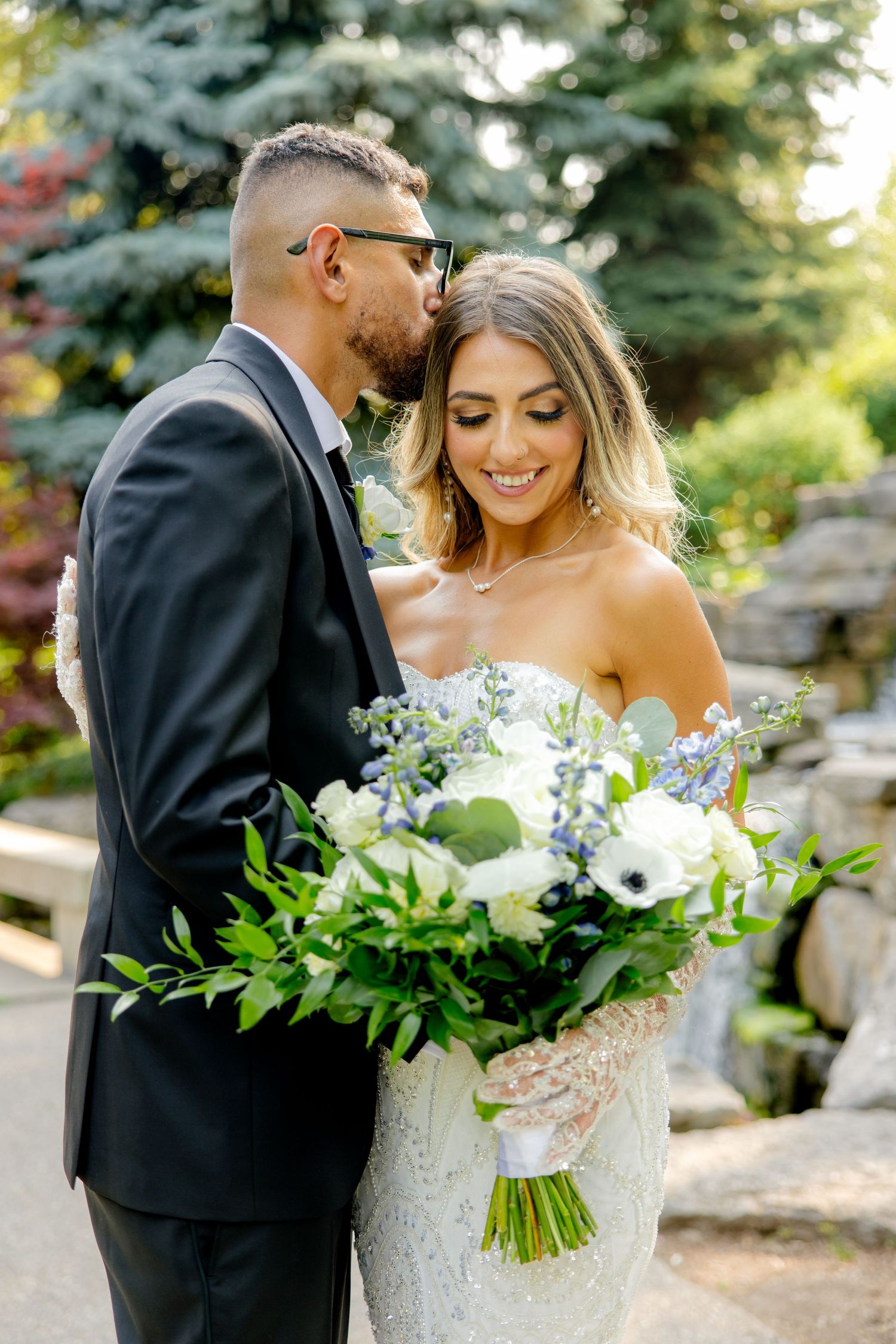A couple shares a sweet moment during their wedding photoshoot next to lush garden landscaping.