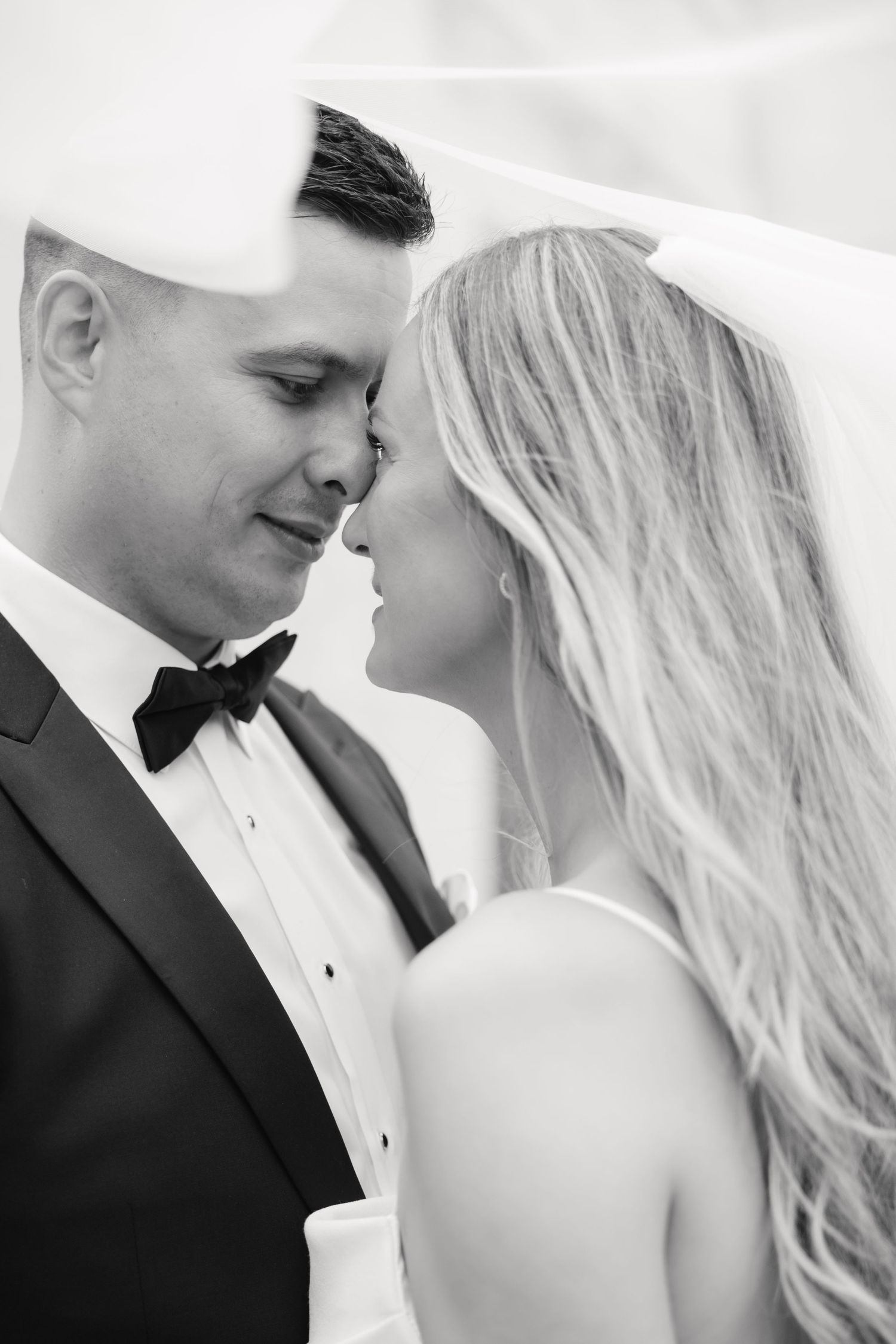 Intimate black and white portrait of newlyweds sharing a romantic moment in formal wedding attire.