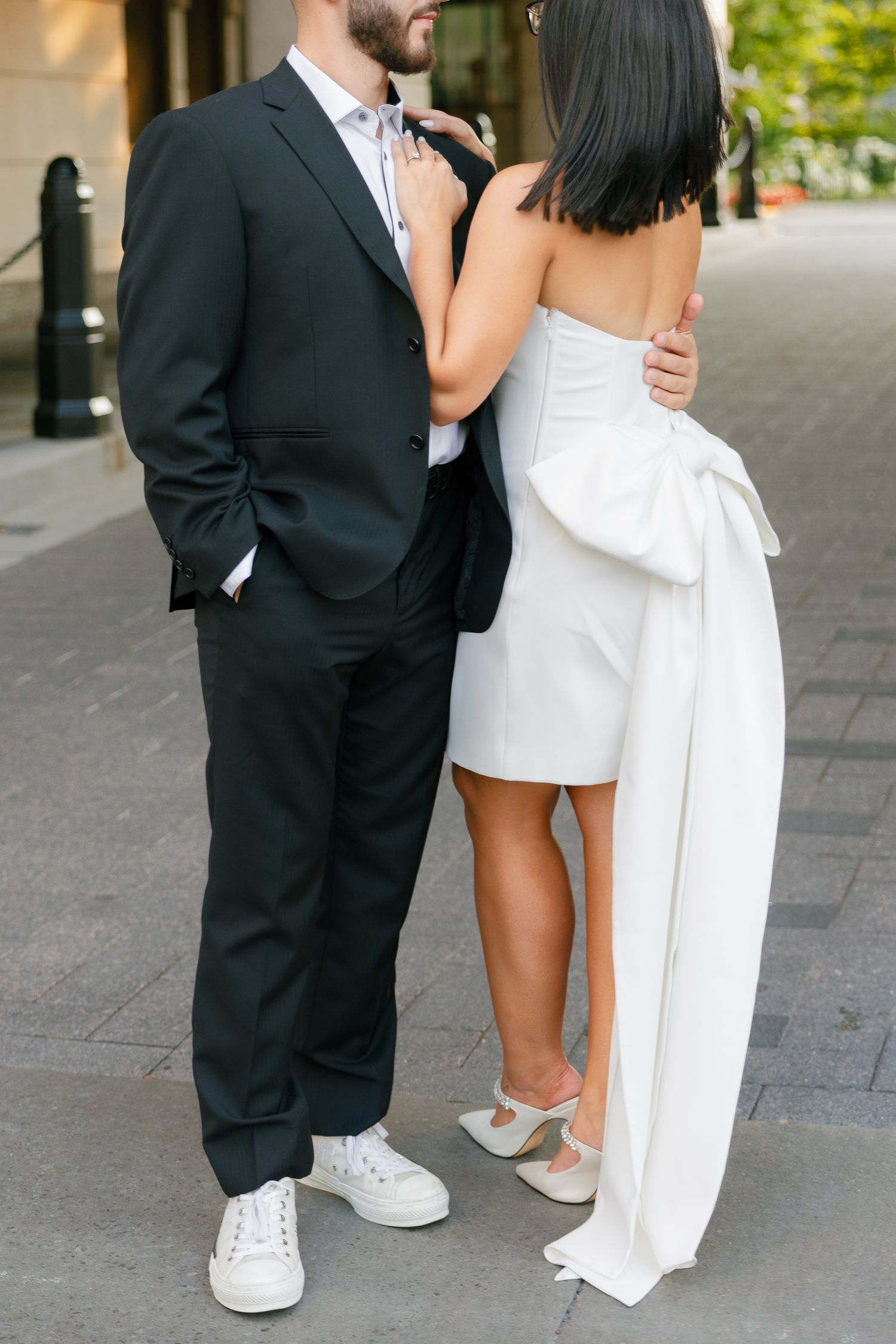 Close-up shot of a couple in contrasting black and white formal wear embracing on an urban sidewalk.