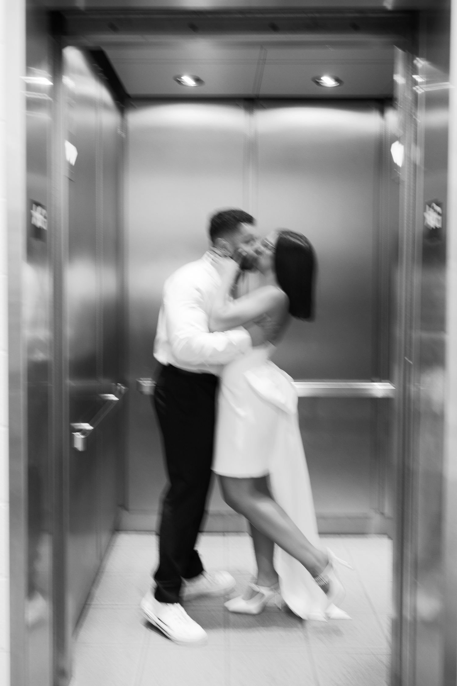 Intimate moment captured between couple in elevator wearing formal attire.