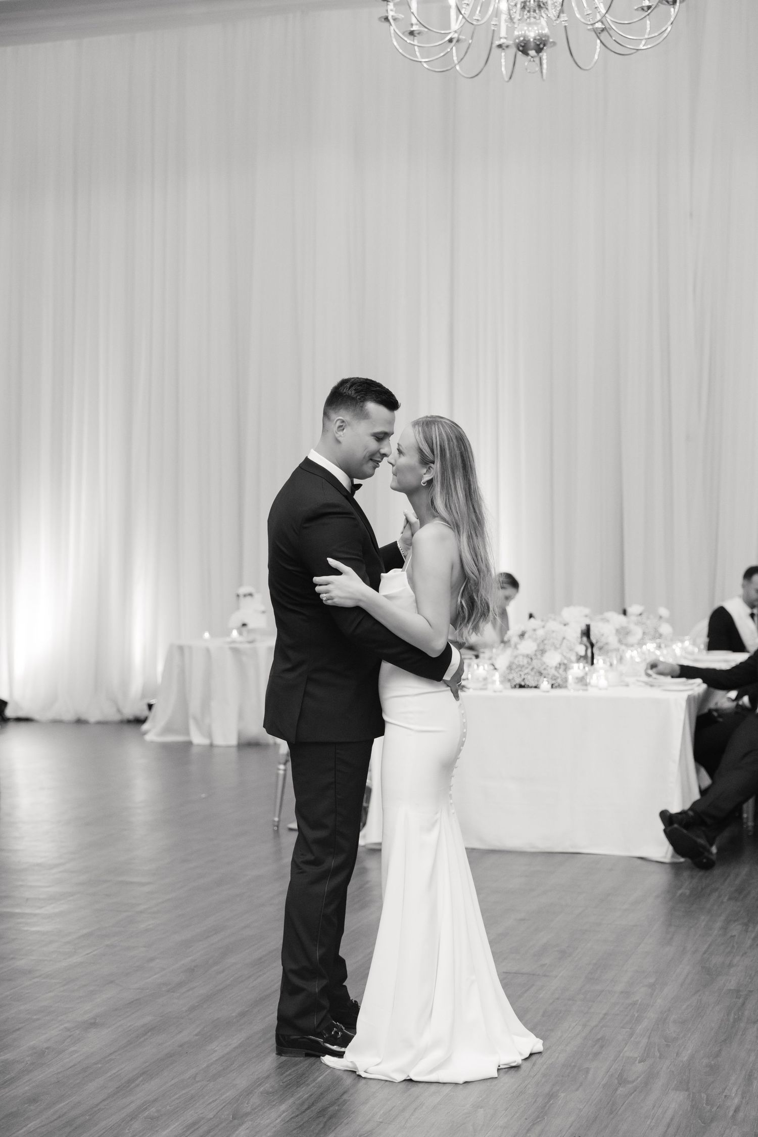 Black and white photo of a couple embracing during their wedding dance on a hardwood floor.