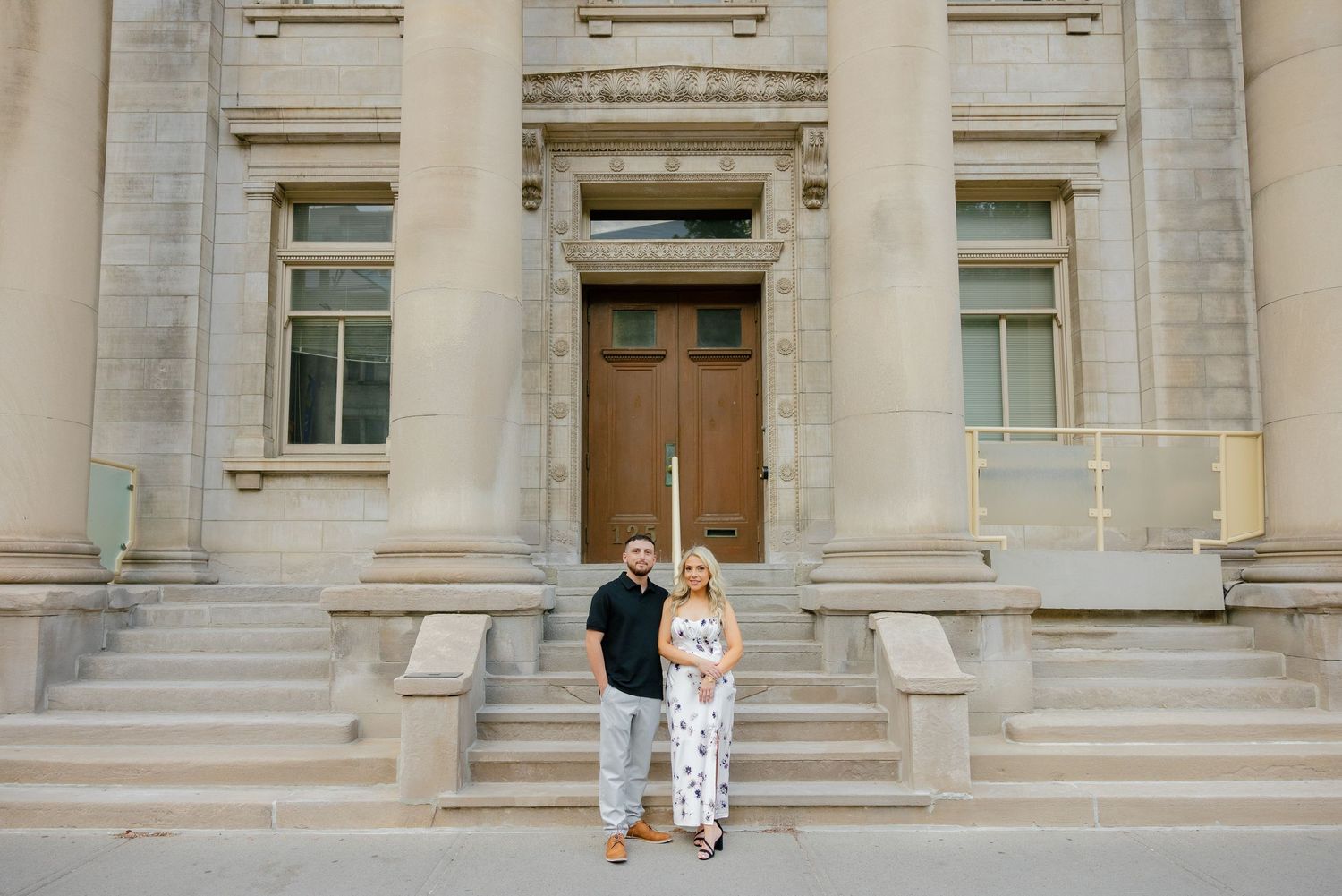 A couple embraces on the steps of a stately building with classical architecture.