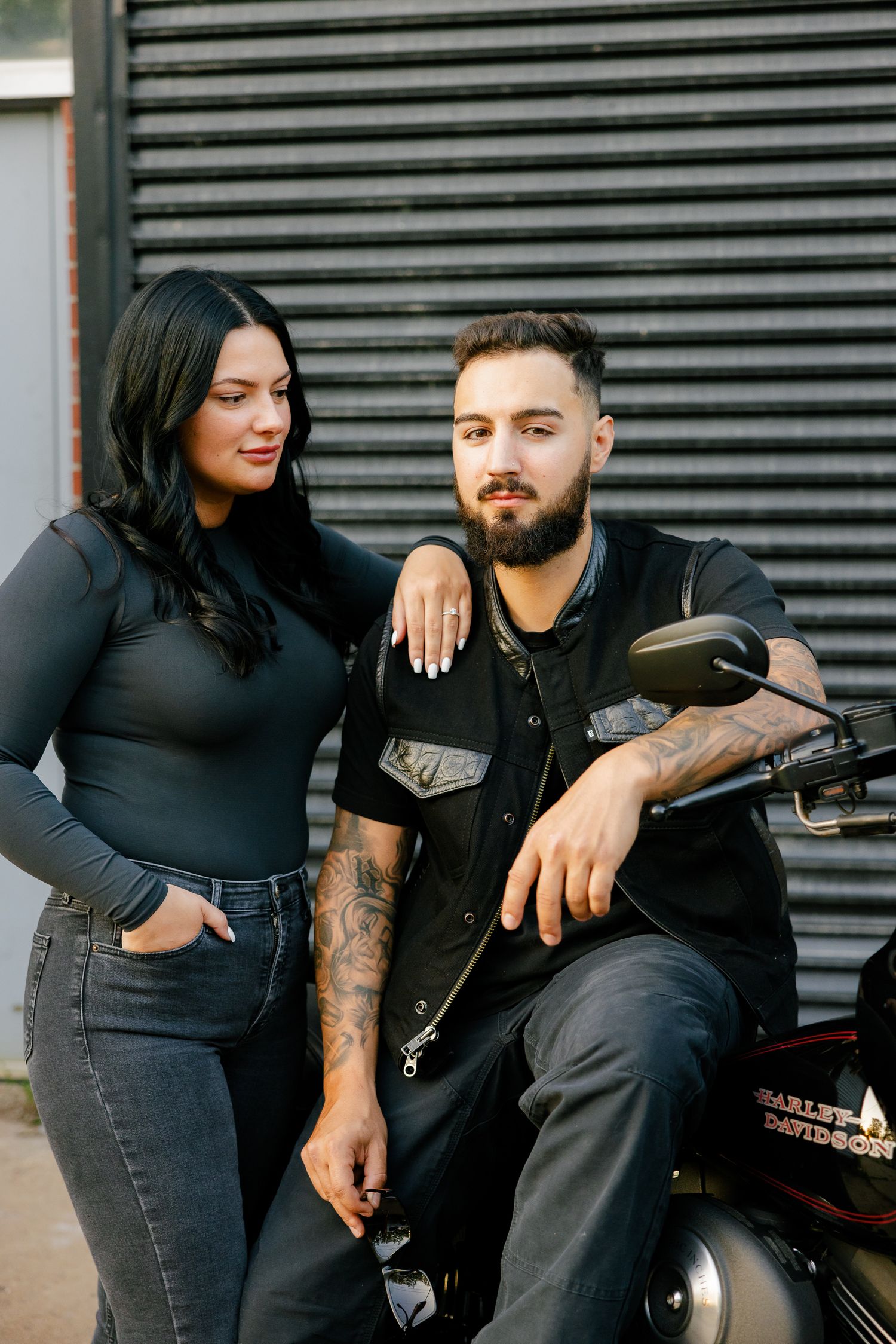 A stylish couple shares an intimate moment while posing with their motorcycle.