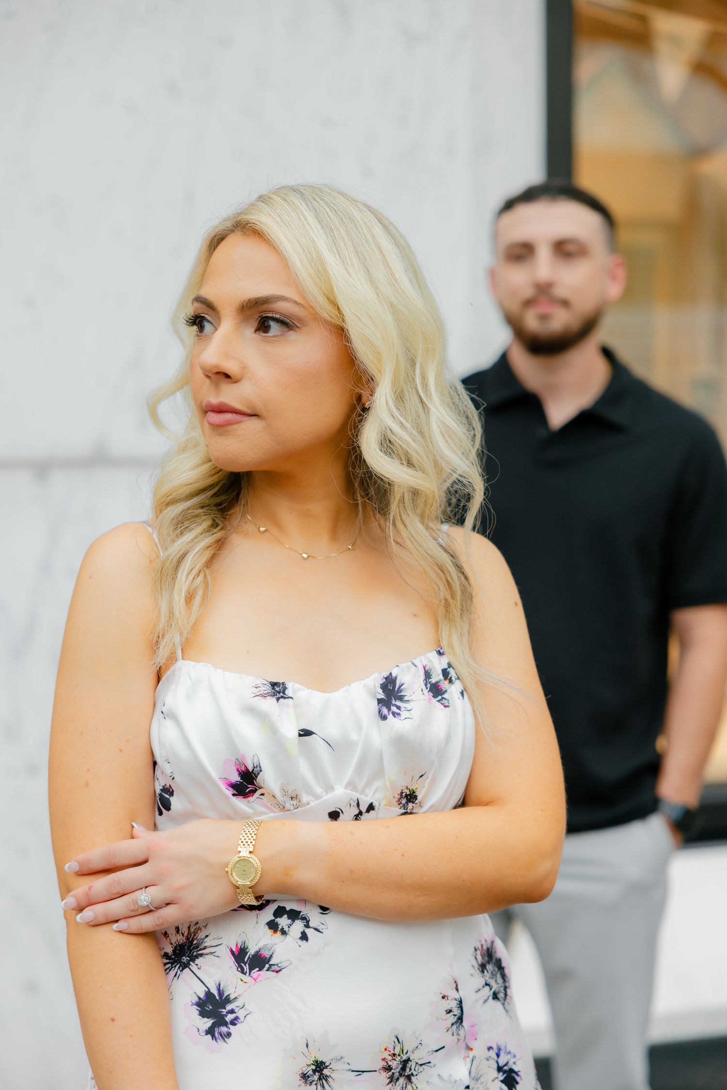A fashionable couple poses in front of a modern storefront with marble walls.