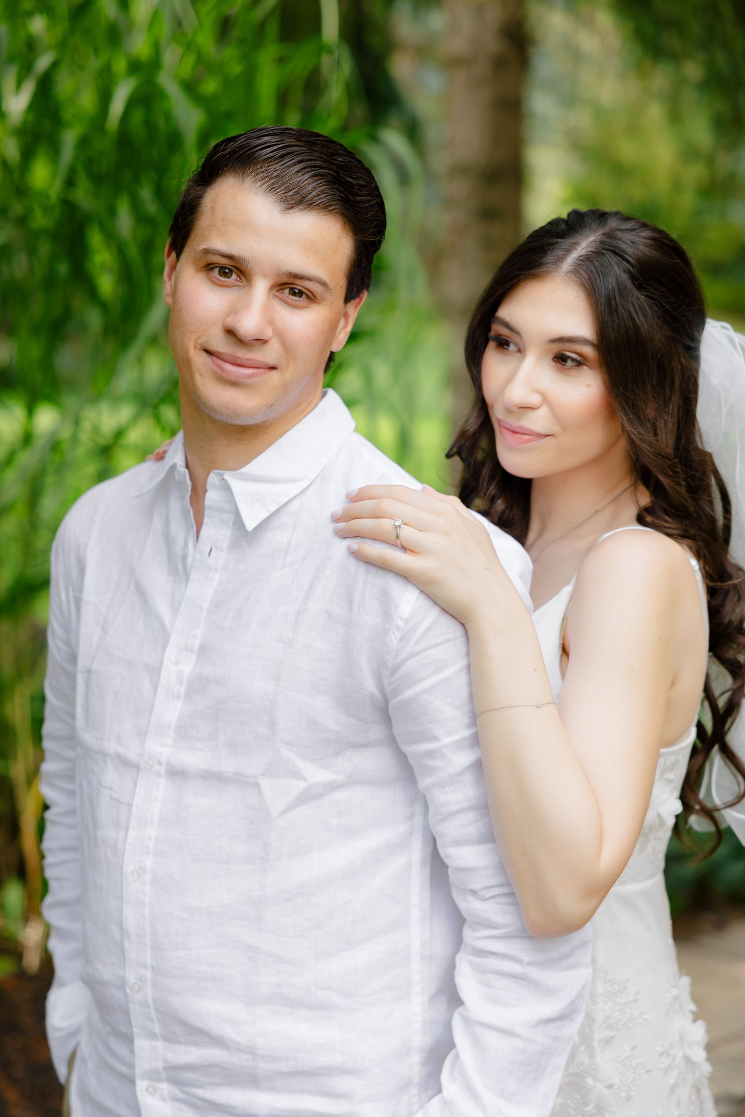 An elegant couple in white clothing poses for their wedding photos in a garden.