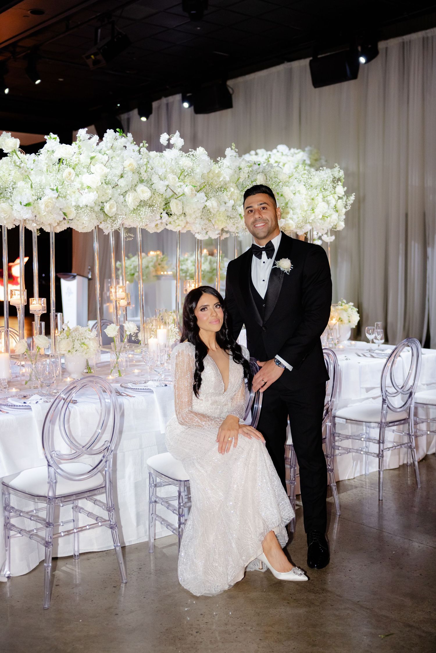 Elegant wedding reception setup with crystal chairs and dramatic white floral arrangements.