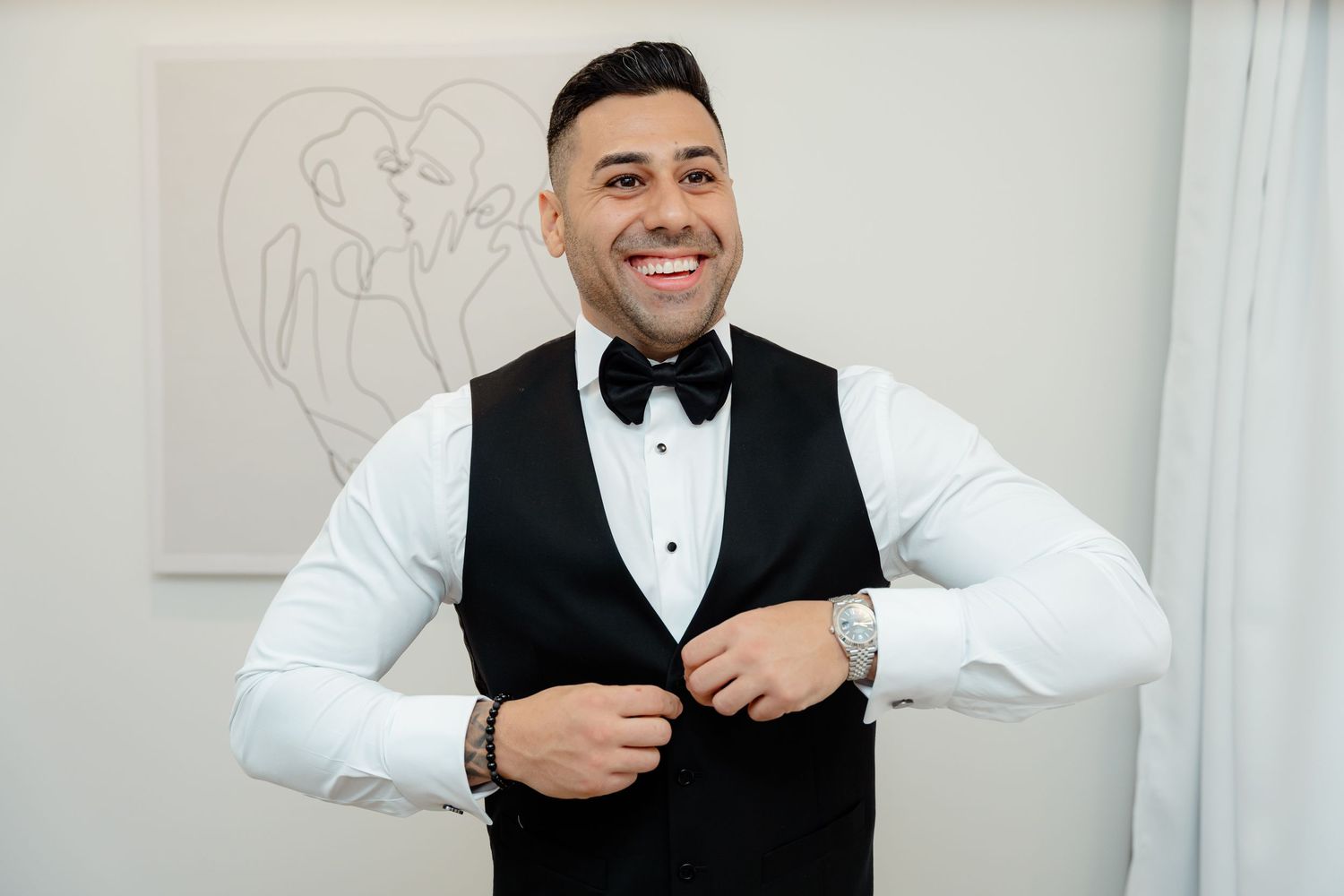 Happy groomsman in formal vest and bow tie adjusting buttons.