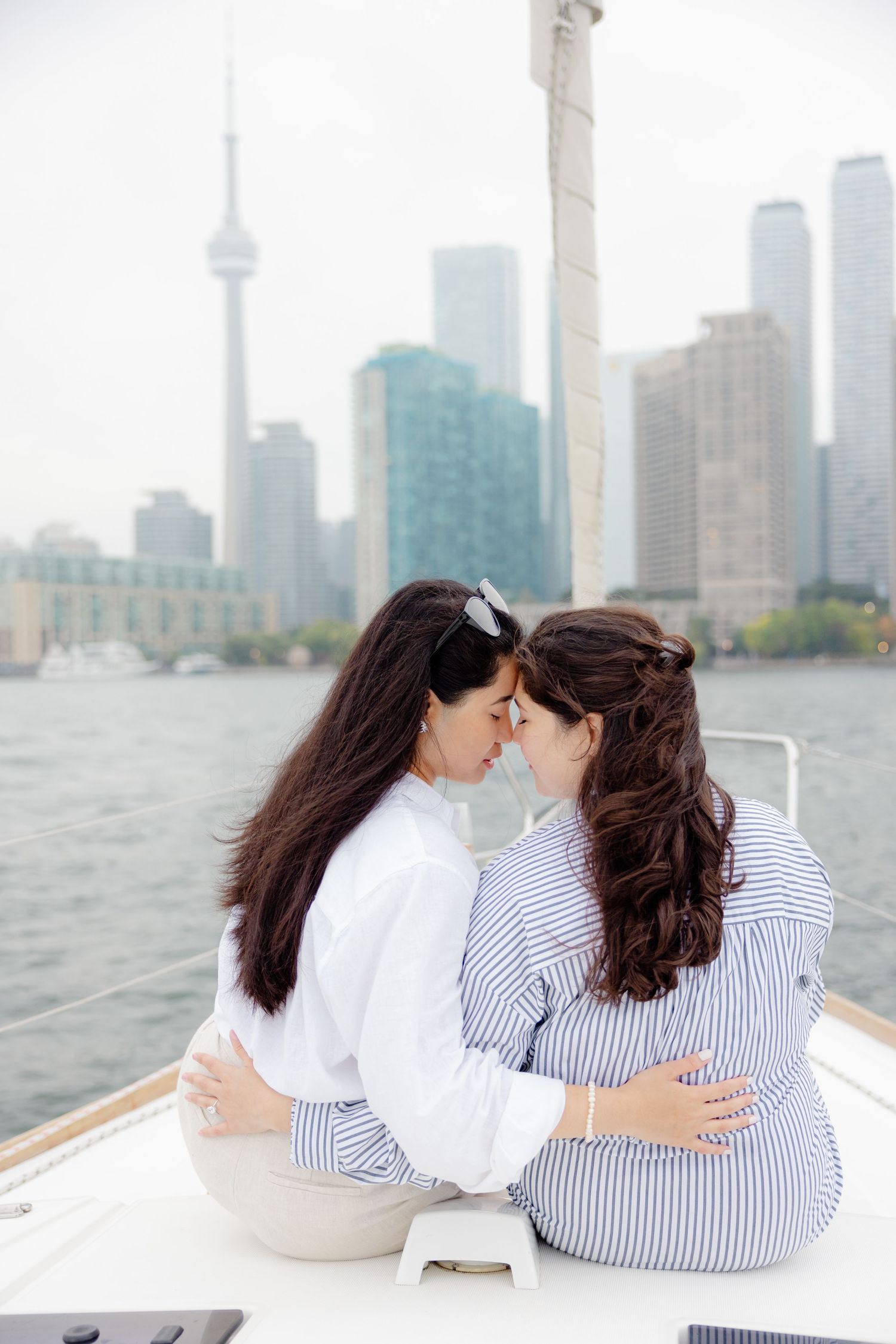 Two people sharing an intimate moment on a boat with the Toronto skyline and CN Tower visible in the background.