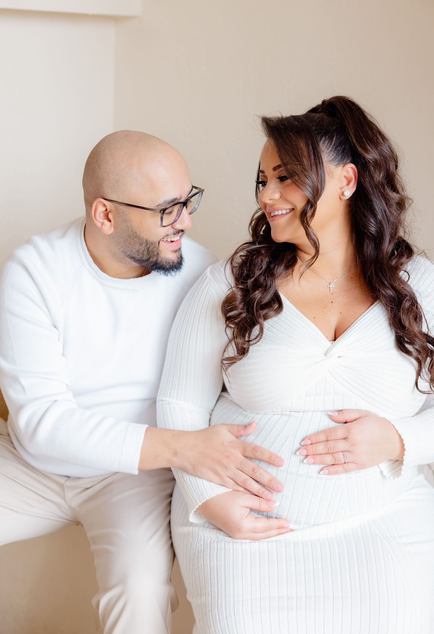 A loving moment between an expecting couple wearing white, sharing tenderness as they embrace the pregnancy together.
