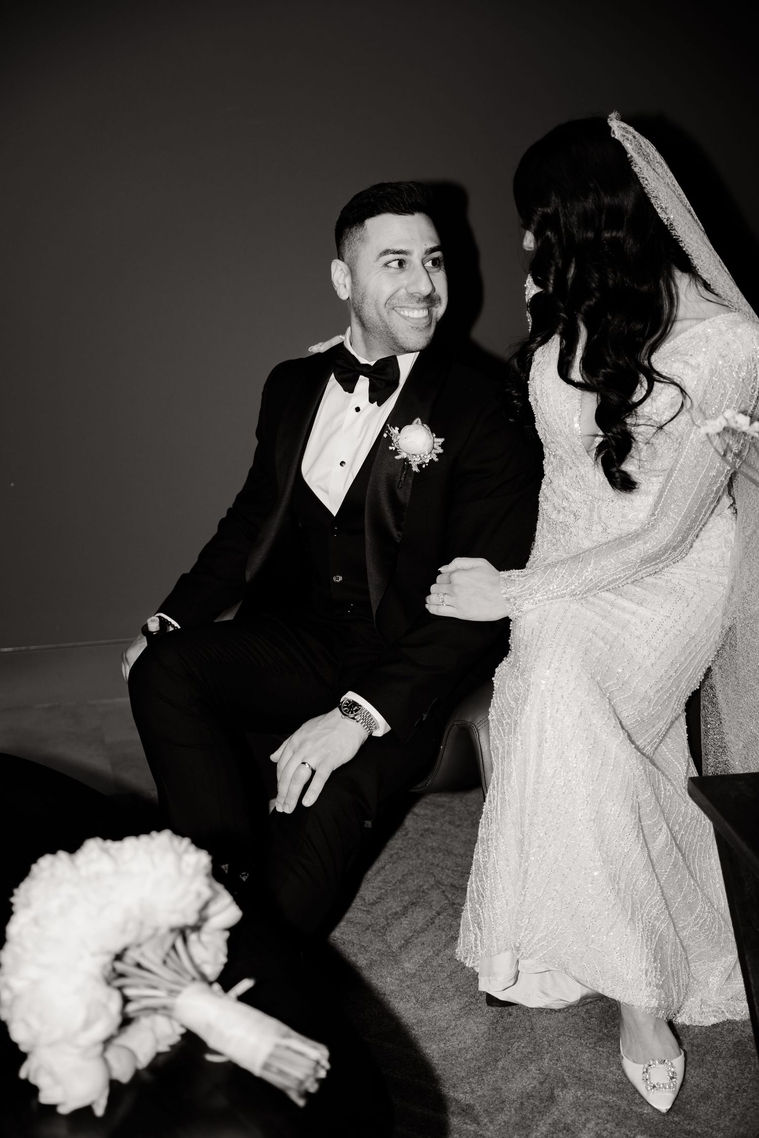 A candid black and white wedding photo showing a couple sharing a joyful moment with a white bouquet on the floor.
