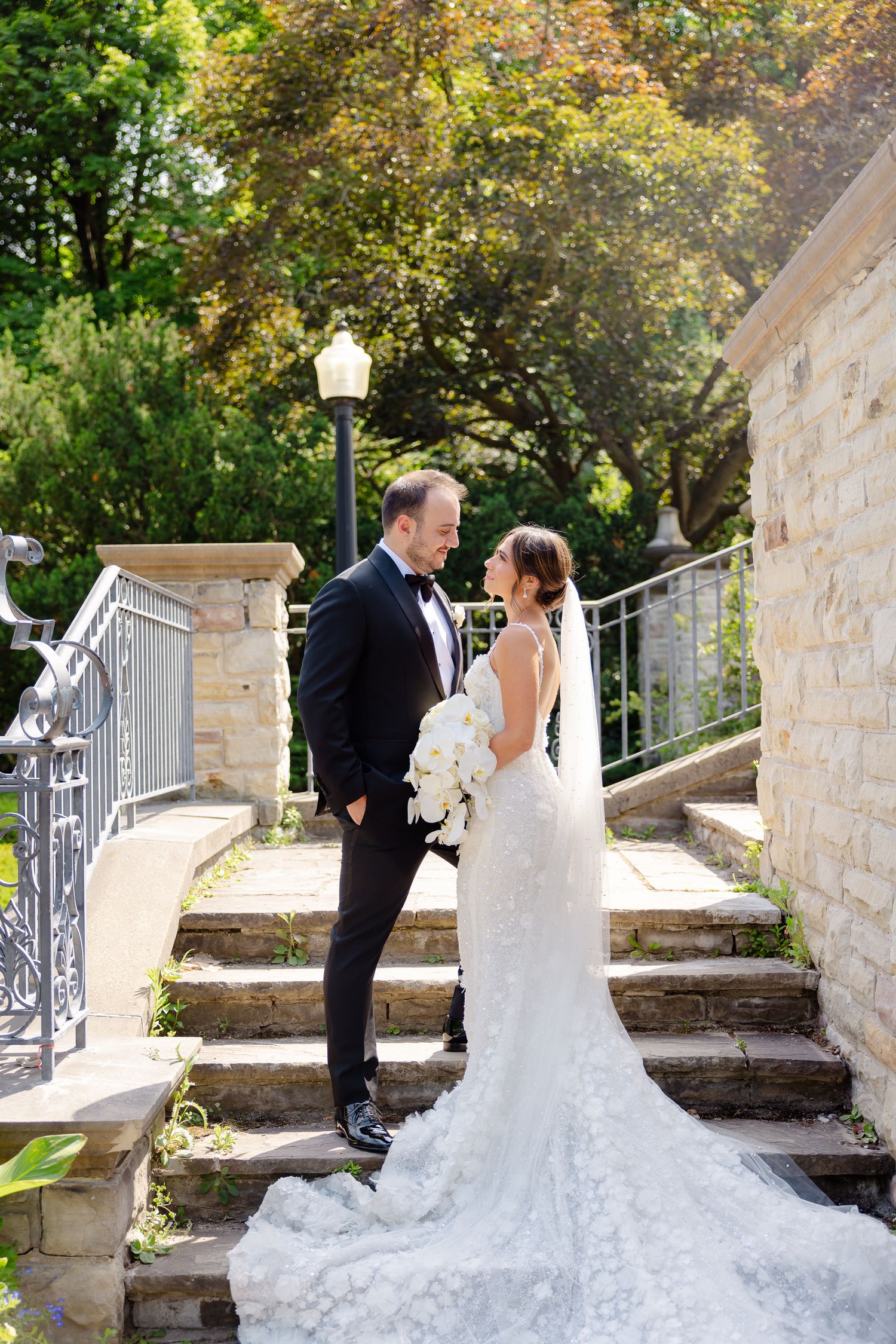 A bride and groom share a romantic moment on a stone staircase surrounded by autumn foliage.