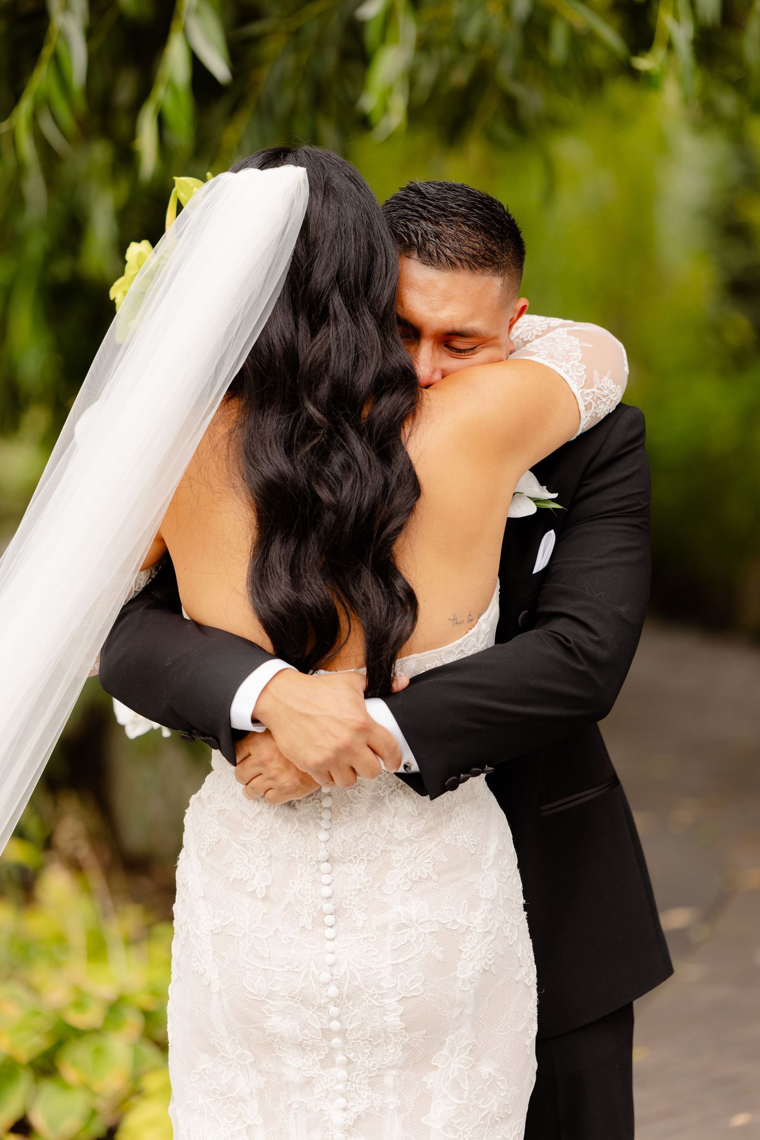 A romantic wedding couple shares intimate kisses in an outdoor garden setting with greenery in the background.