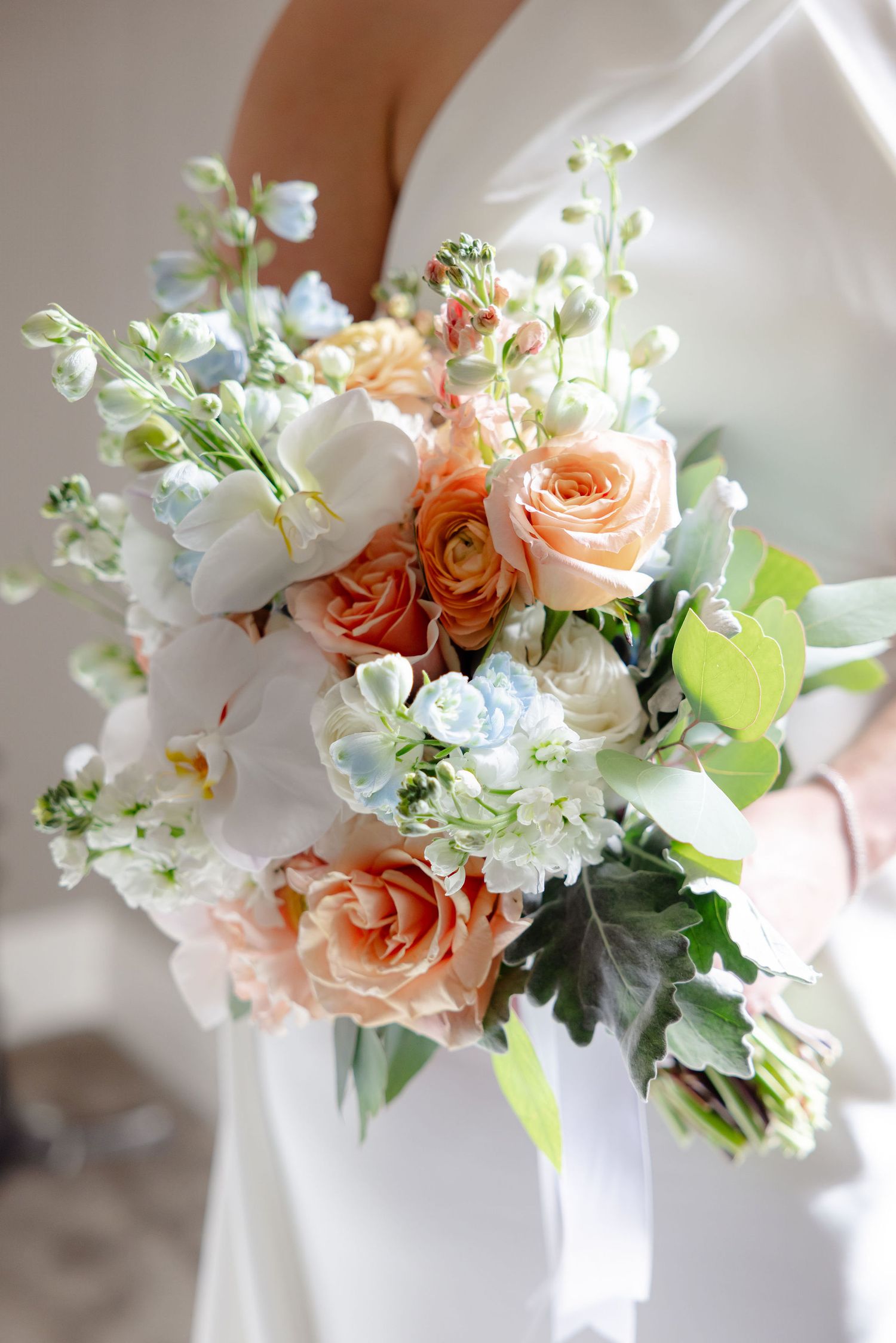 A delicate floral arrangement featuring peach roses, white flowers and greenery against a light background.