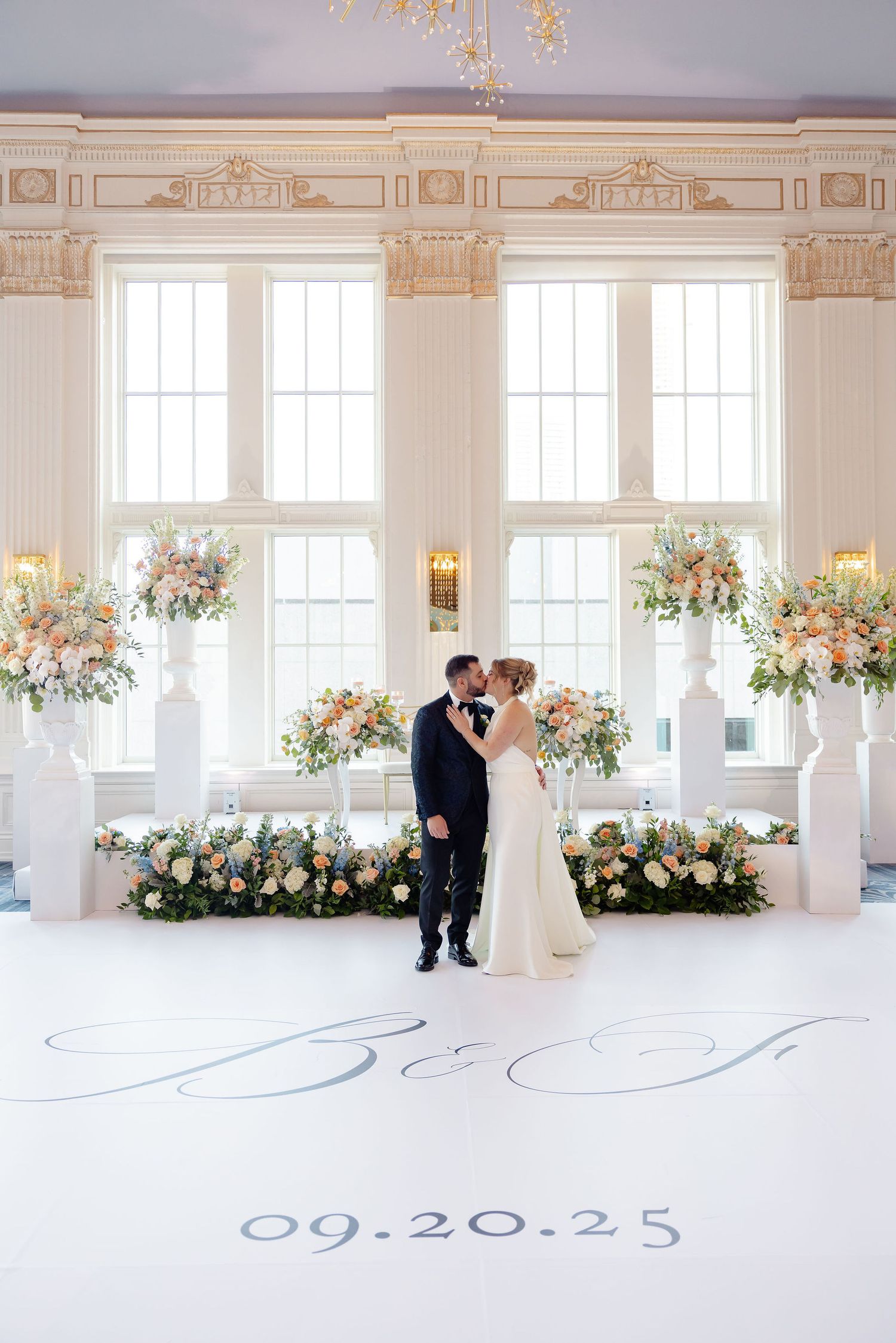 Elegant white wedding venue with floral arrangements and a date written on the floor reading 09.20.25.