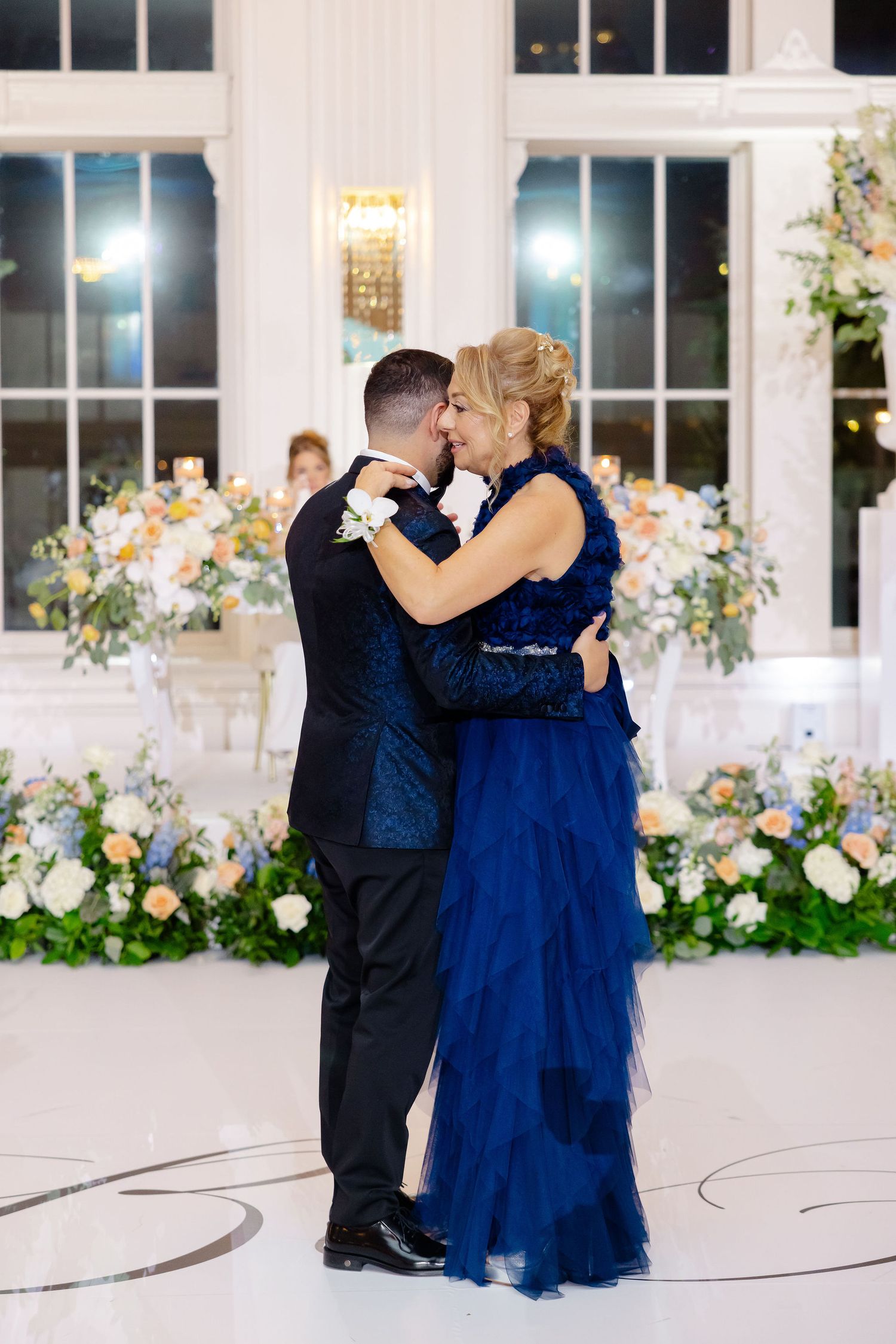 Couples dancing at an elegant wedding reception with floral decorations and large windows in the background.