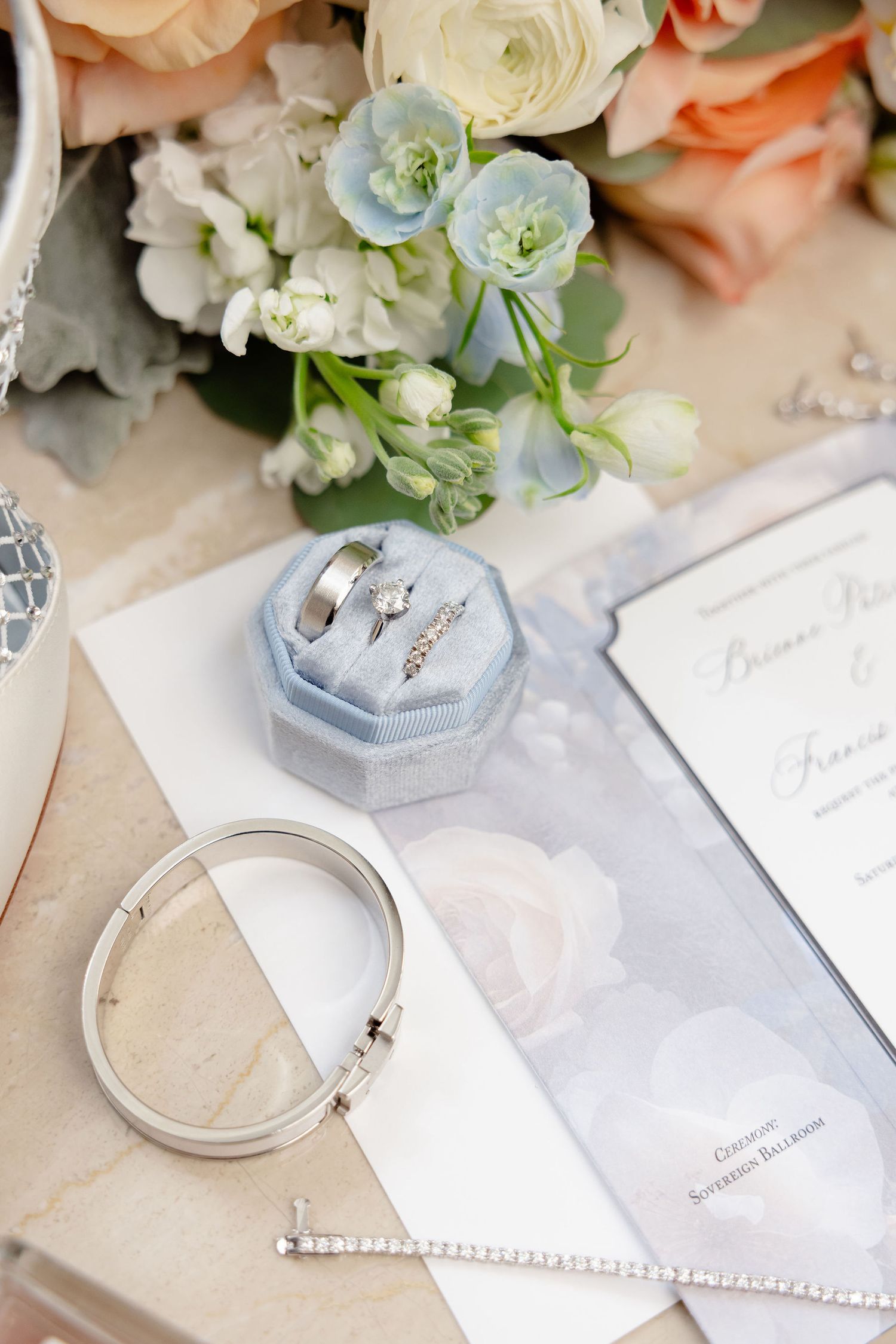 Wedding flat lay with roses, stationery, and jewelry in soft pastel colors.
