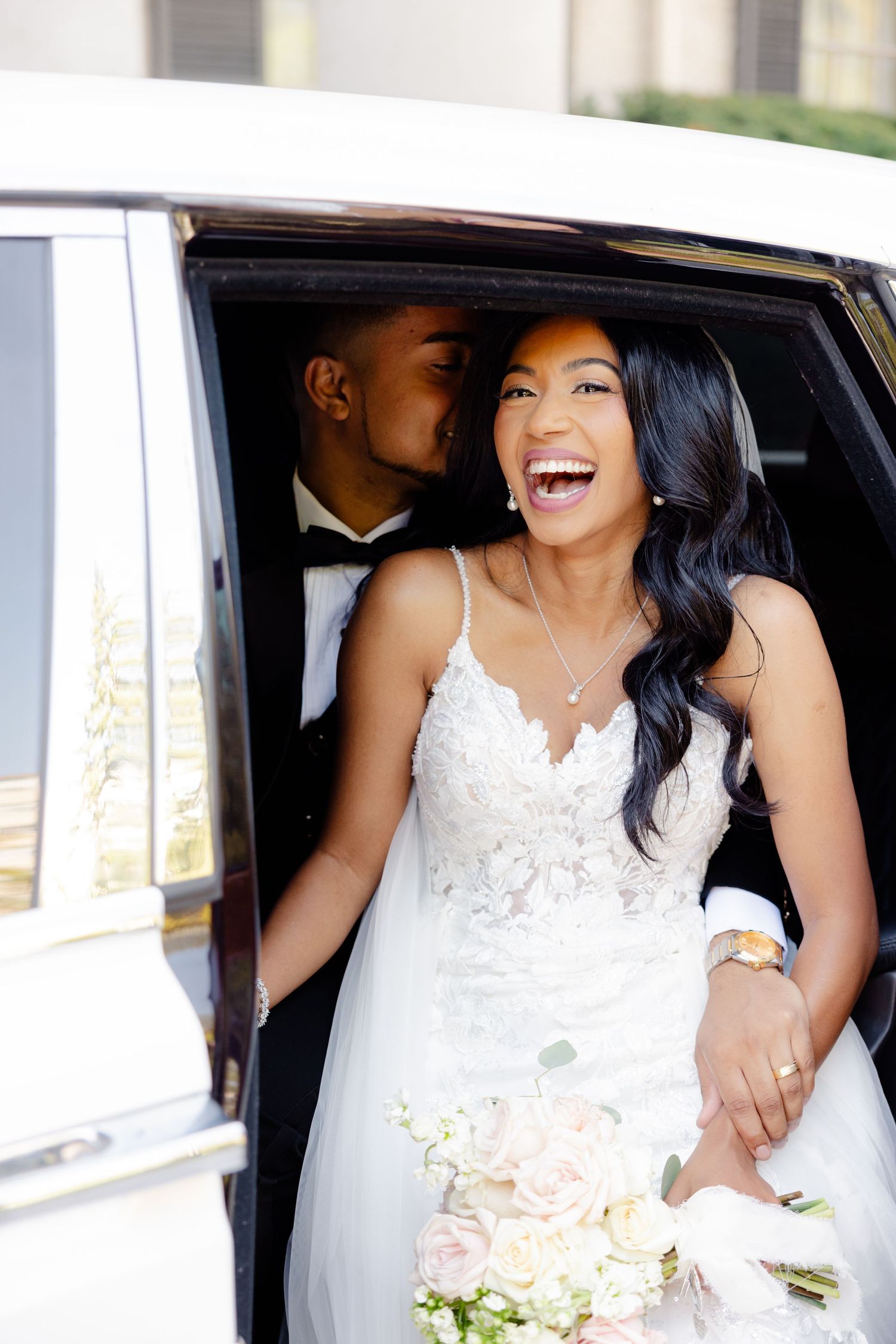 Happy couple sharing a candid moment in their wedding attire inside a car.