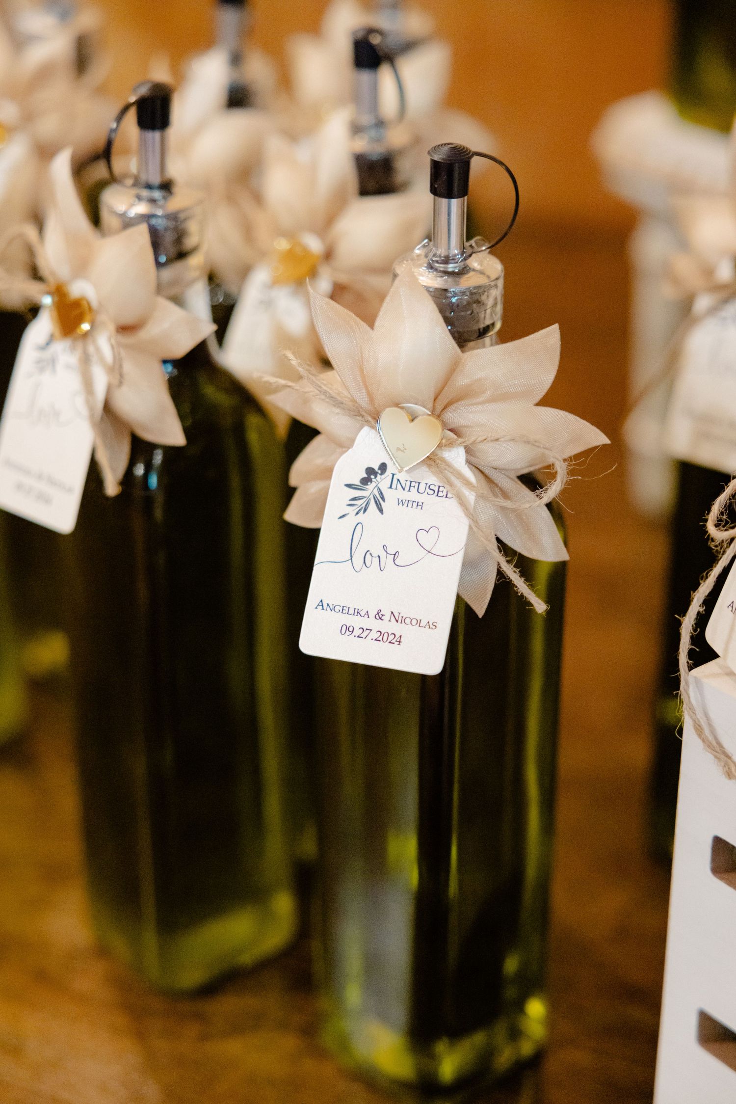 Glass bottles of olive oil decorated with white paper flowers and wedding favor tags.
