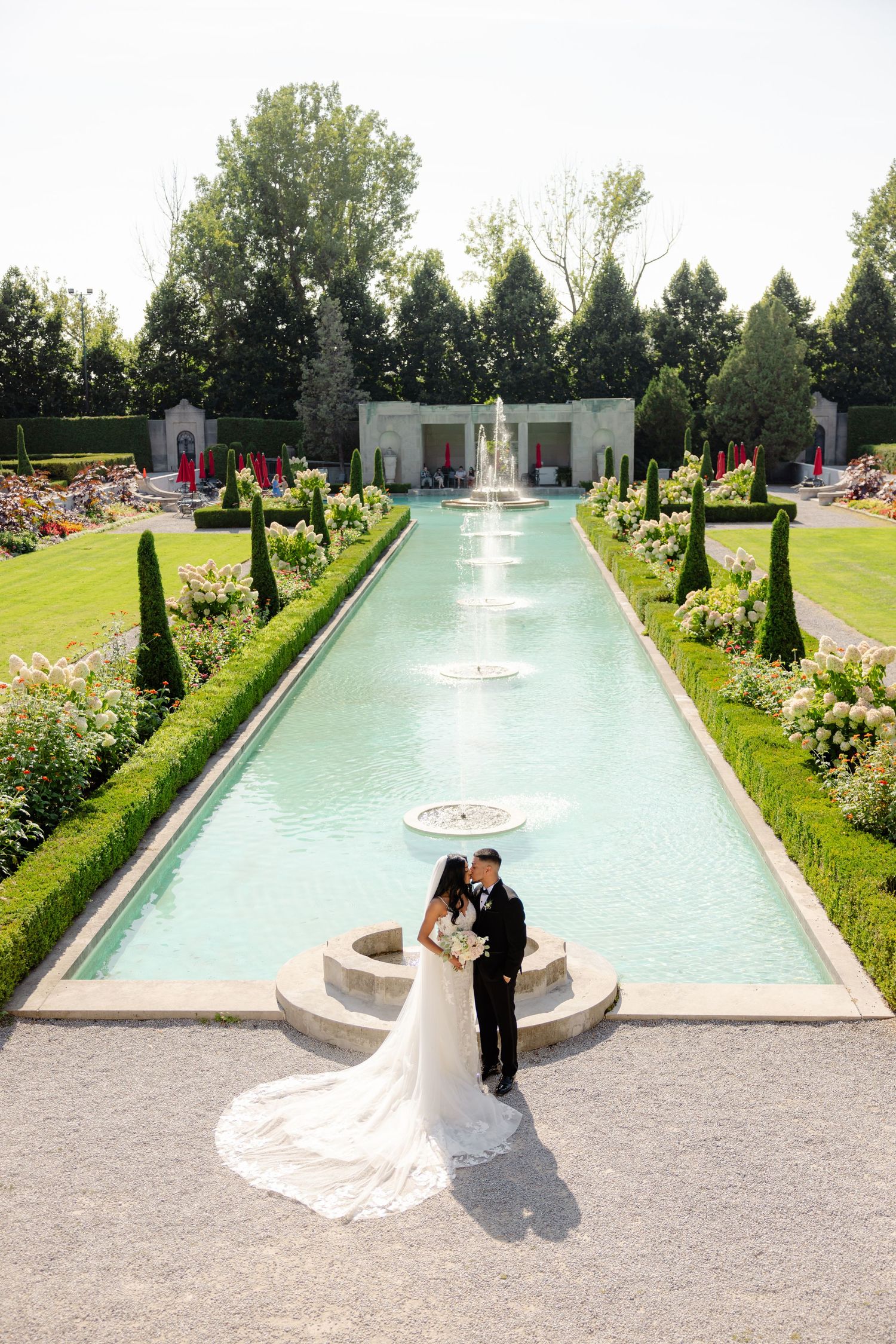 Elegant wedding portrait at a formal garden fountain with perfectly manicured landscaping.
