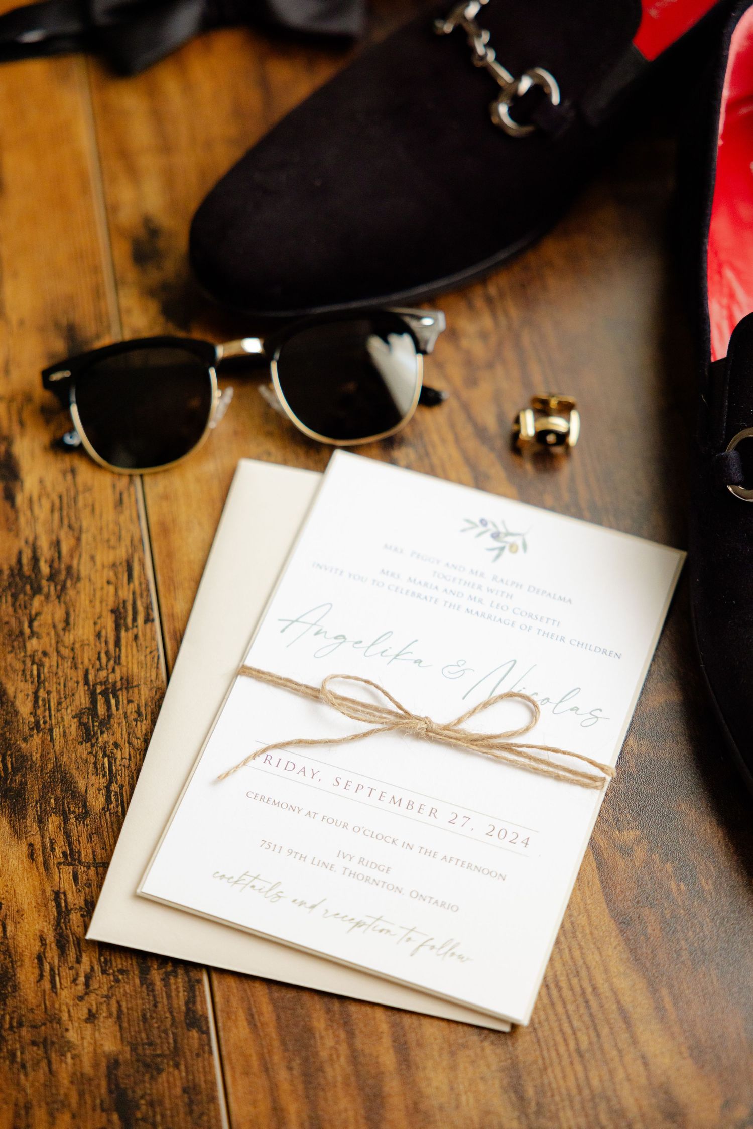 Elegant wedding invitation tied with twine displayed with sunglasses on rustic wooden table.