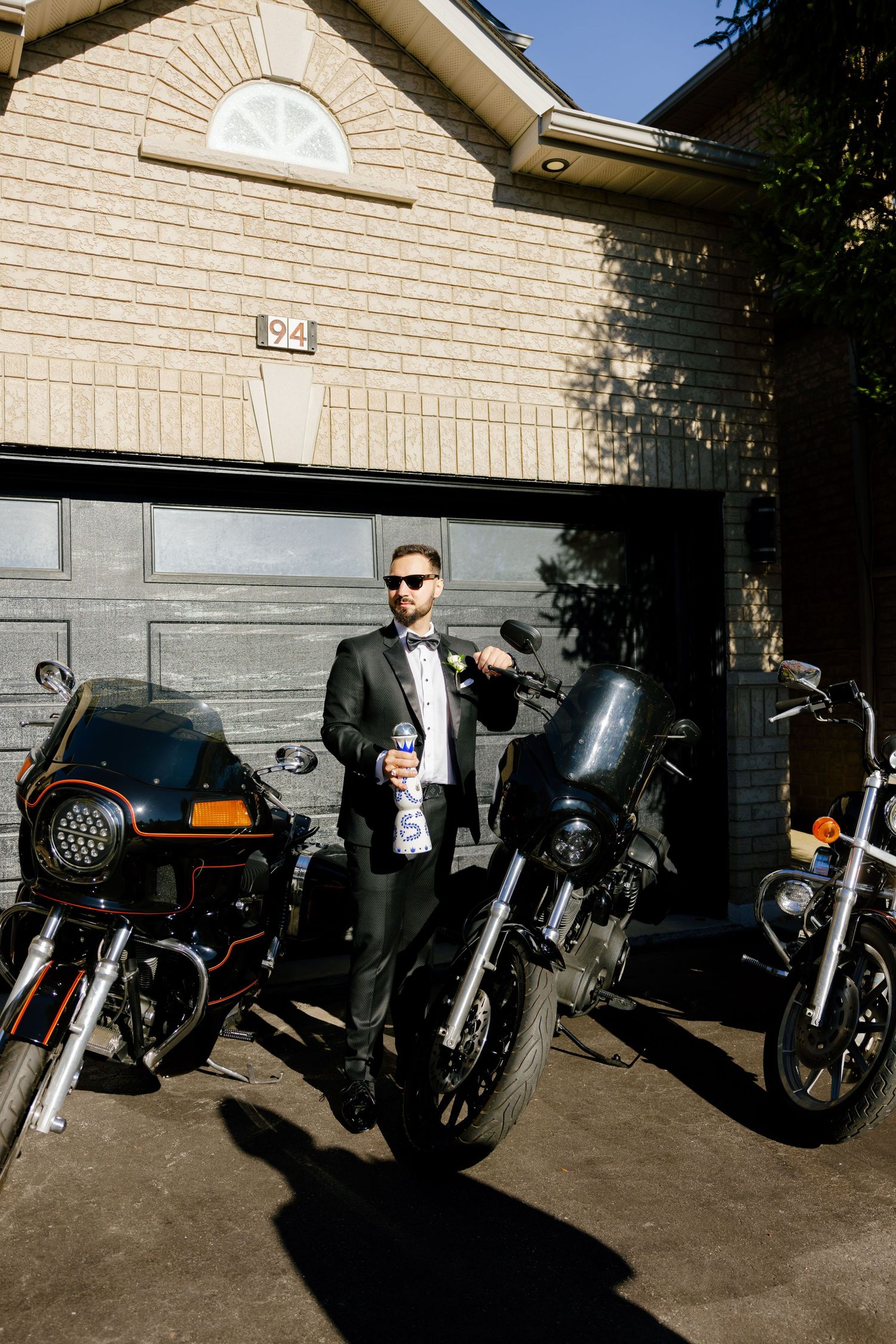 A formally dressed person stands between motorcycles holding a beverage outside.