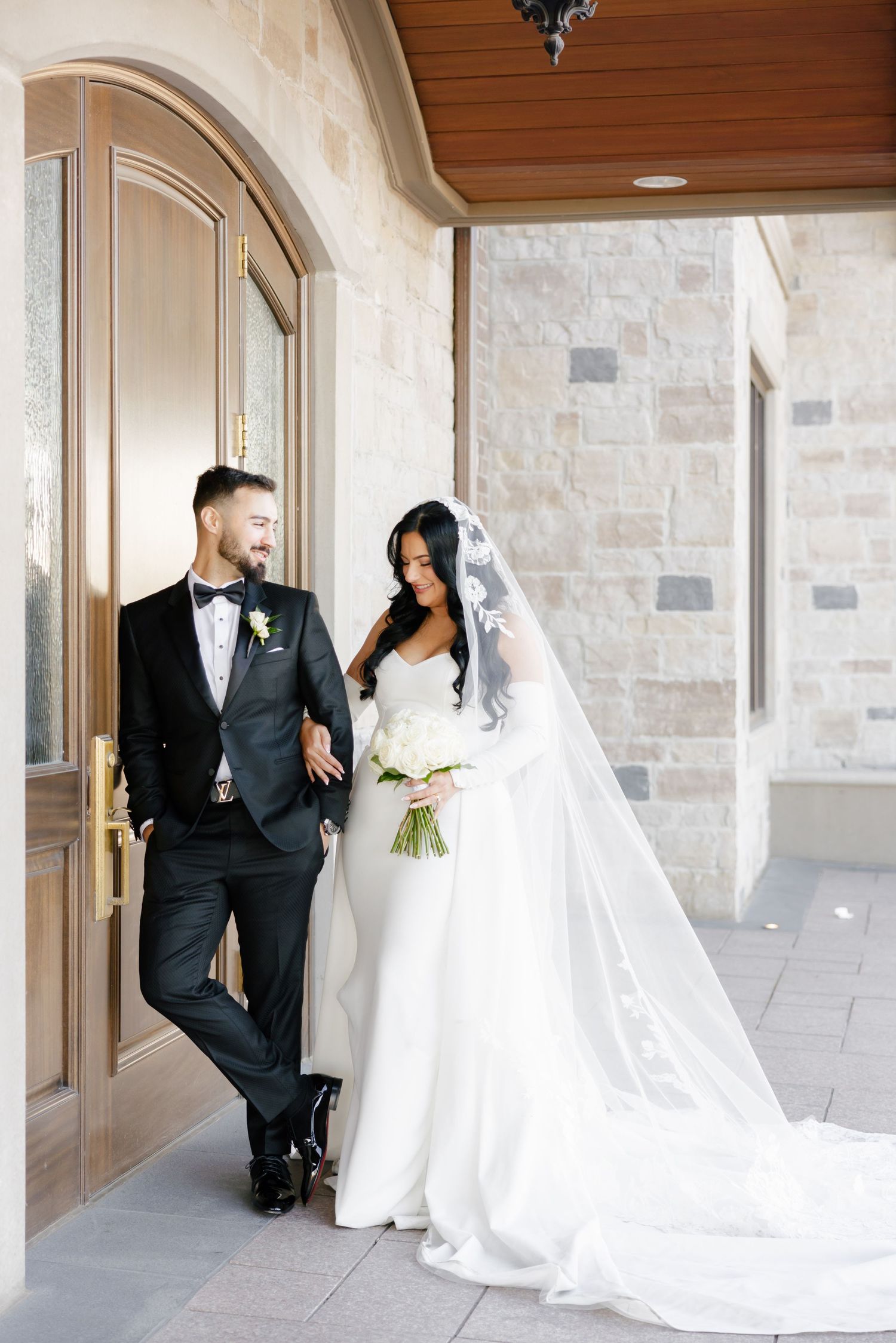 Newlyweds stand in archway with bride's long train flowing behind her white gown.