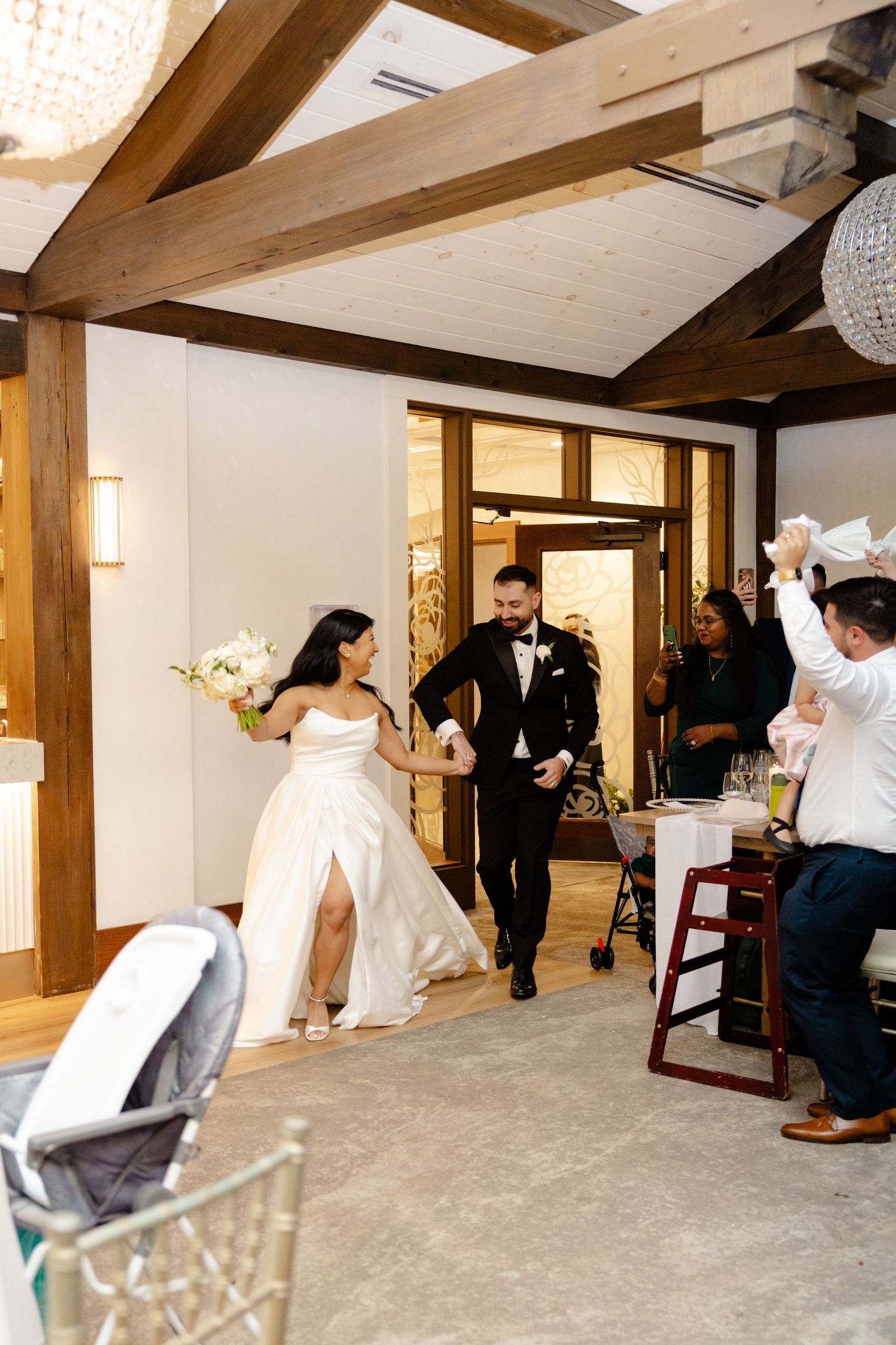 Wedding celebration entrance moment in rustic venue with wooden beams and crystal chandeliers.