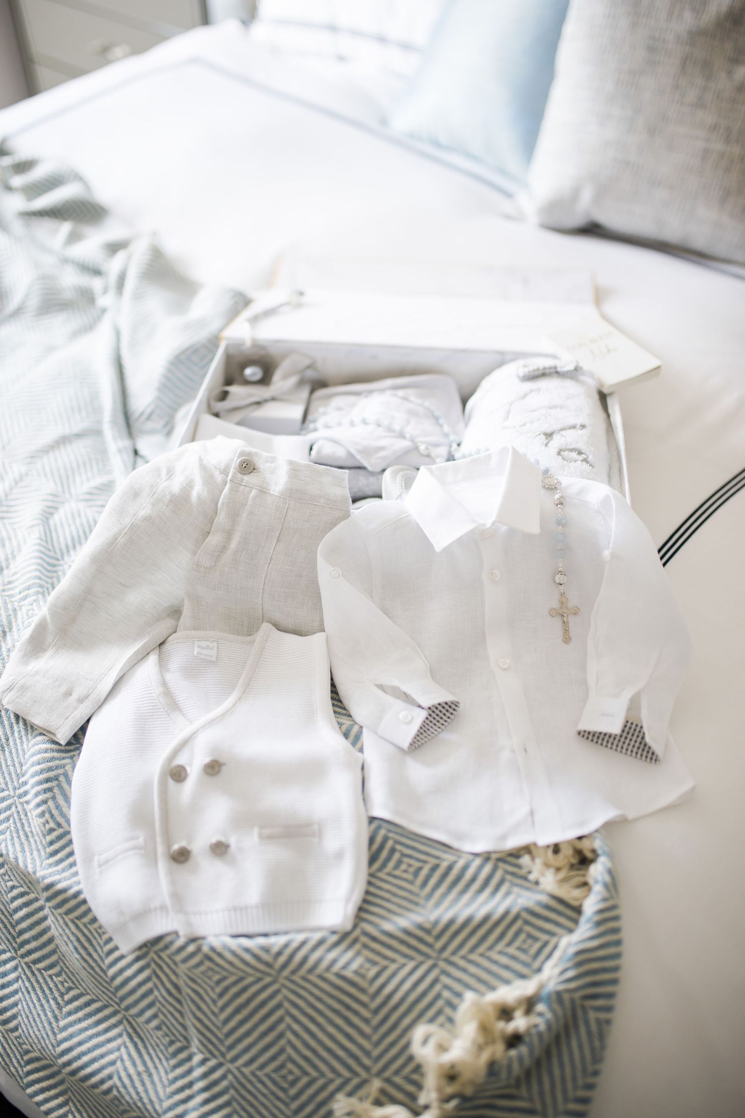 White baptismal clothing and accessories arranged on blue and white bedding.