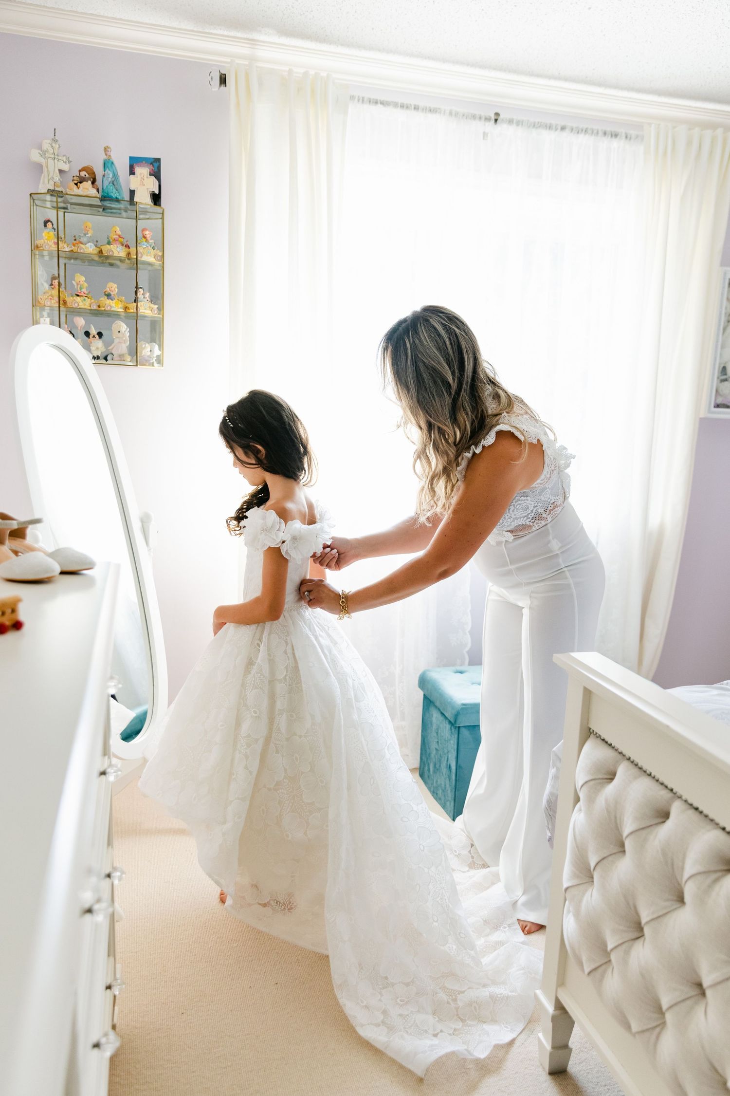 Wedding dress fitting session reflected in full-length mirror with decorative shelf in background.
