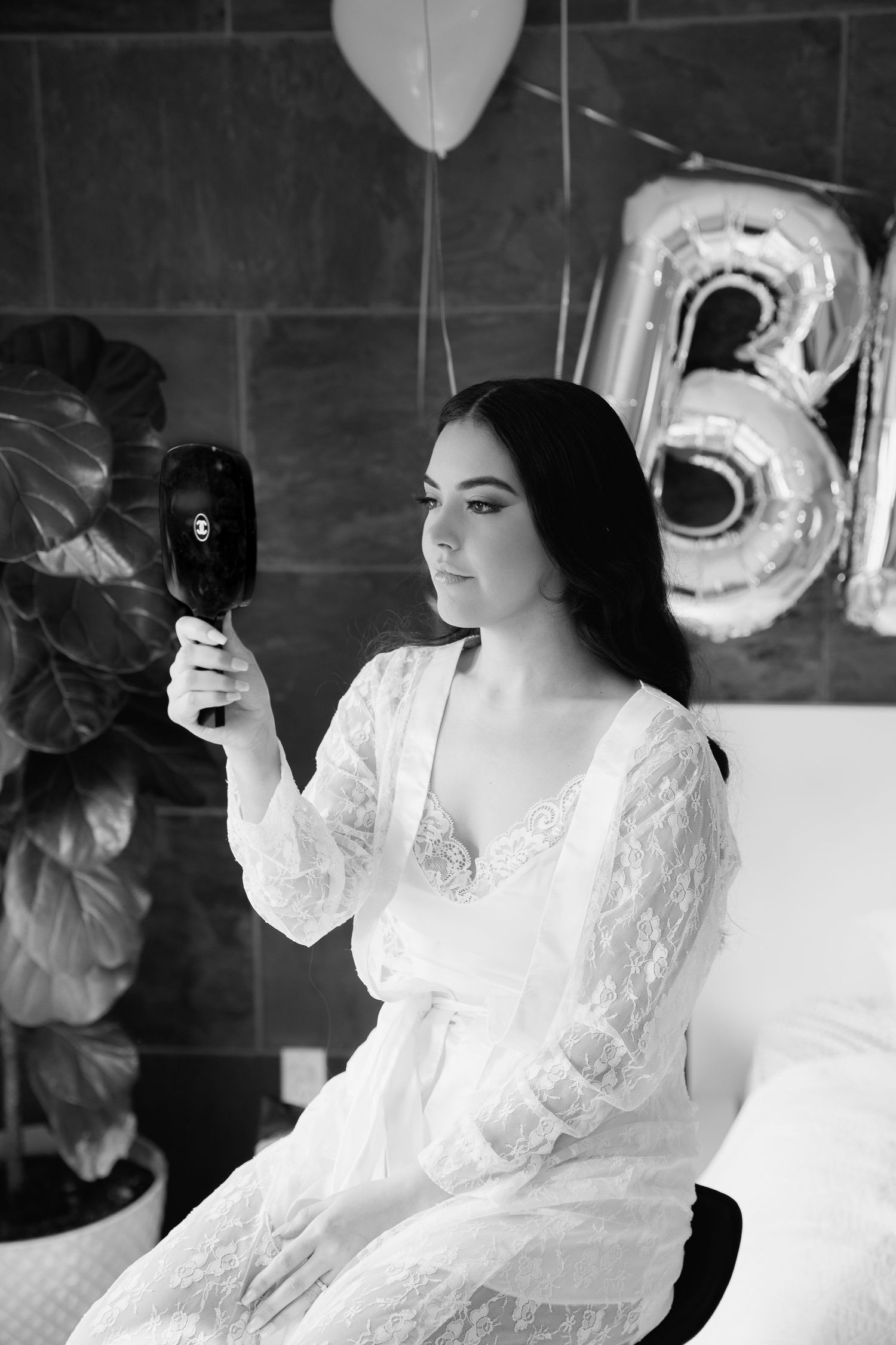 Black and white portrait of bride in lace robe with balloons in background.