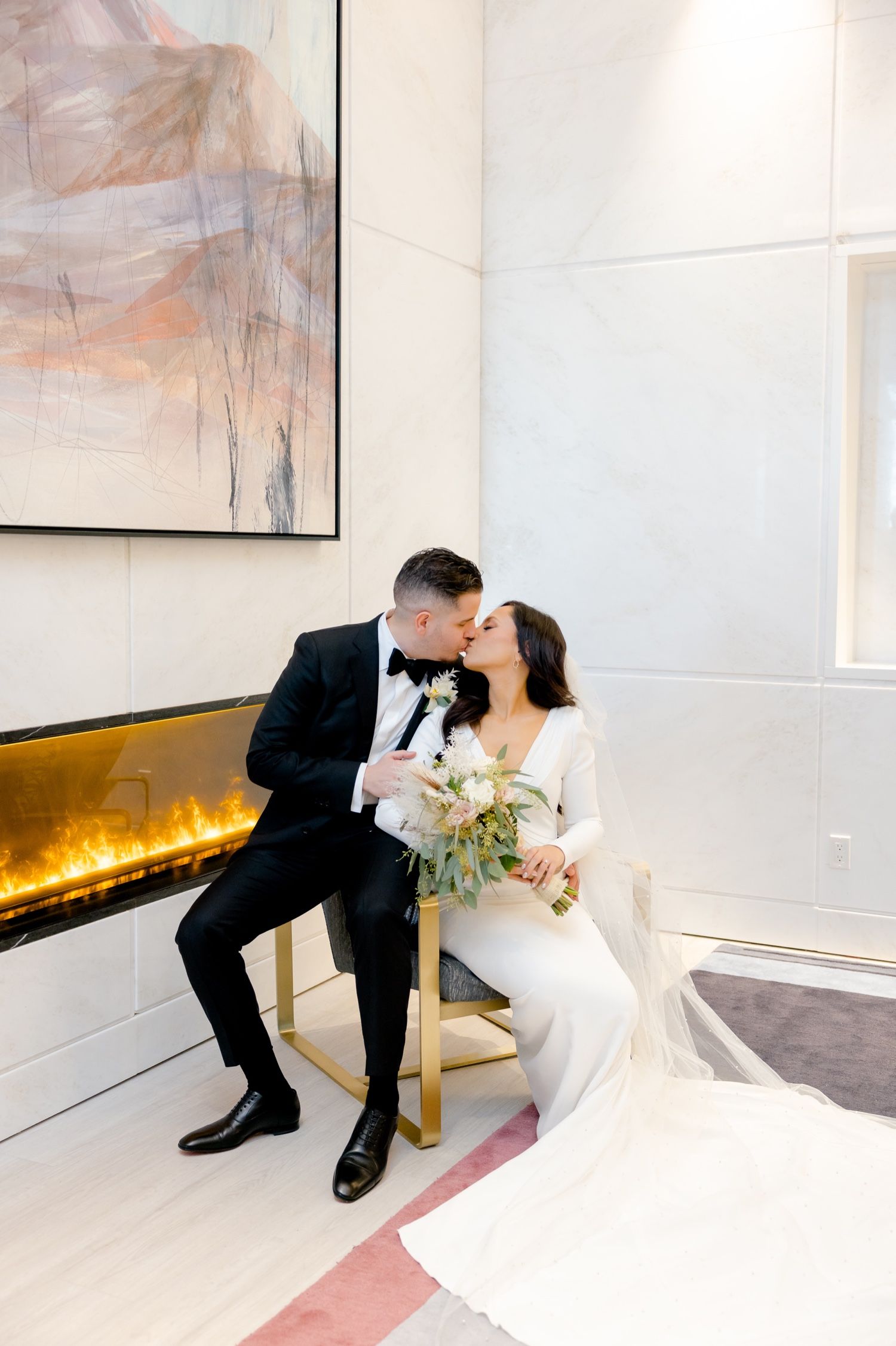 Romantic wedding couple shares tender moment beside modern fireplace with abstract artwork.