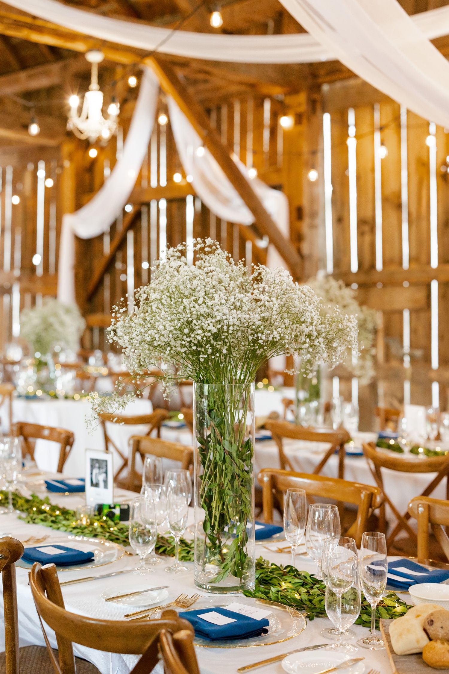 Rustic barn interior decorated with white draping and baby's breath centerpieces for wedding reception.