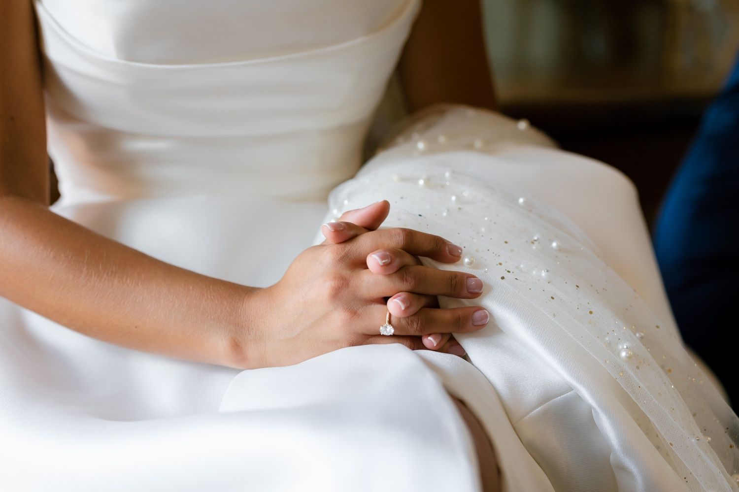 Detail shot of clasped hands on white wedding dress fabric showing sparkly details.
