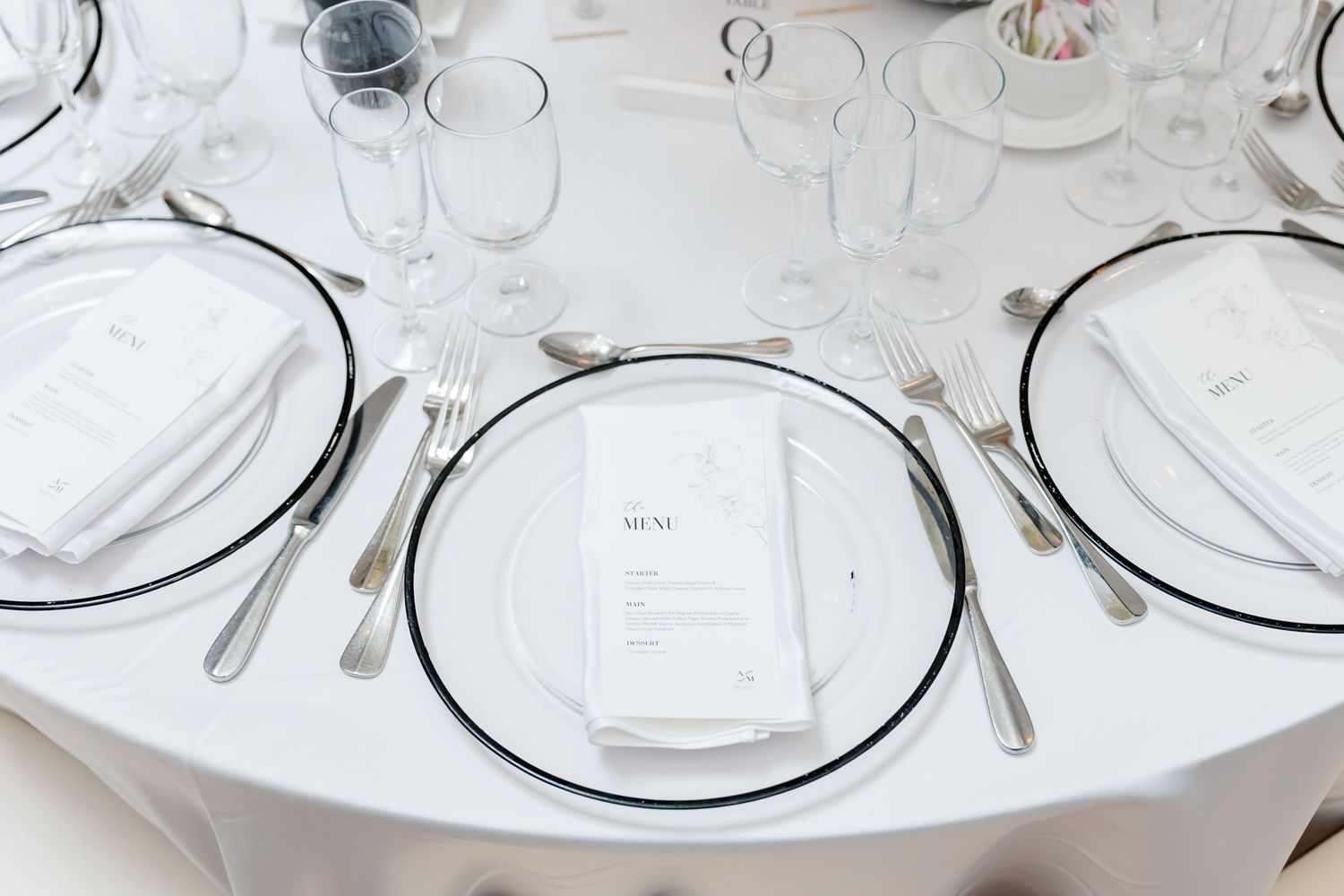 Elegant place setting with clear charger plates and classic silverware on white tablecloth.