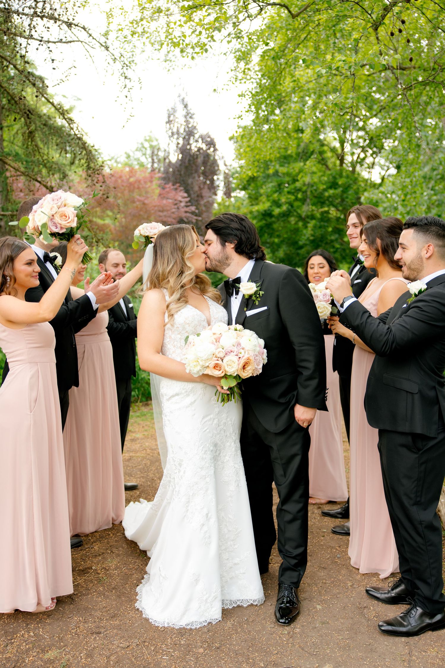 Wedding party cheers and celebrates as newlyweds share romantic moment on garden path.